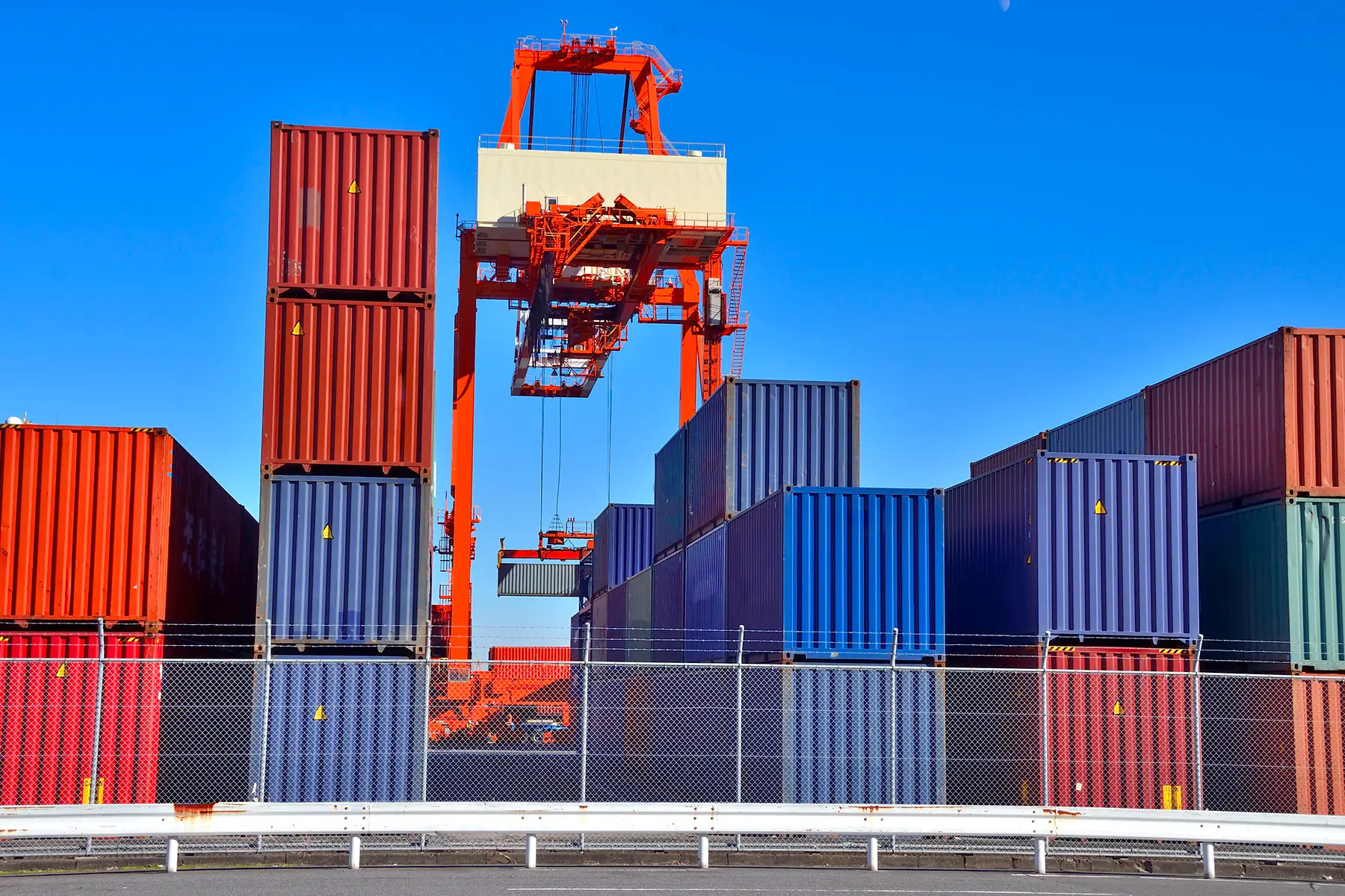 Red and blue shipping containers at a port on a sunny day