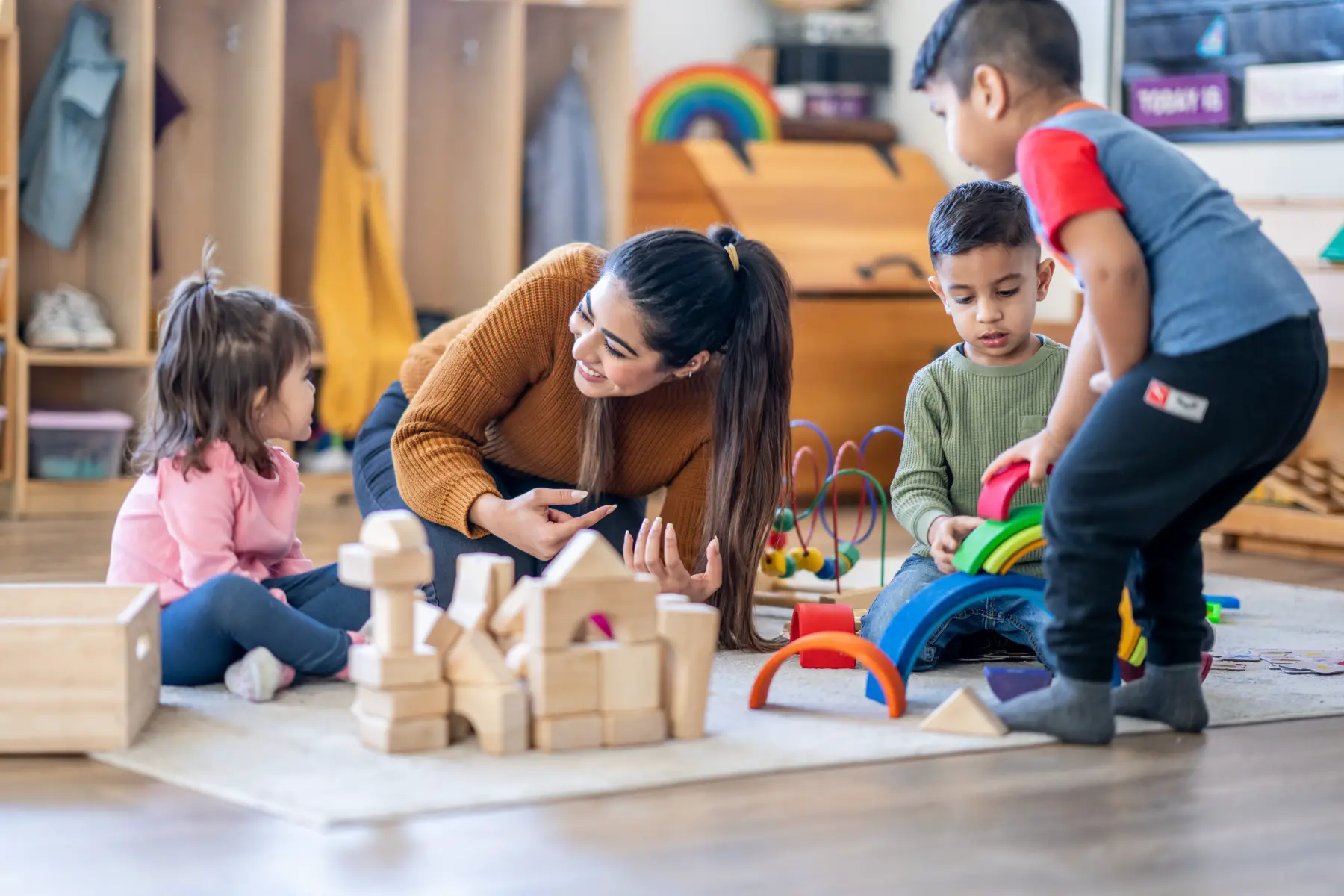 a kindergarten teacher sitting on the floor with a group of mixed-race children playing with building blocks