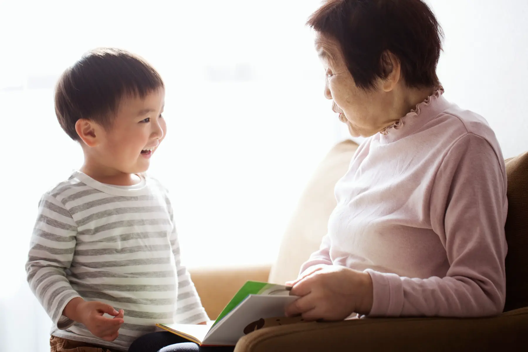 an older Japanese woman looking after a young boy, she sits in a chair and reads him a story