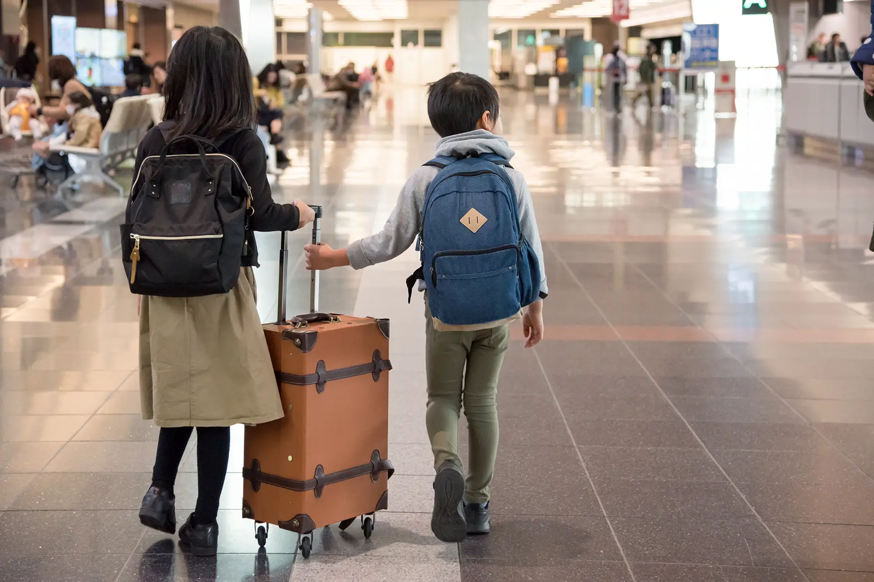 Siblings (brother and sister) walking around an airport with their luggage
