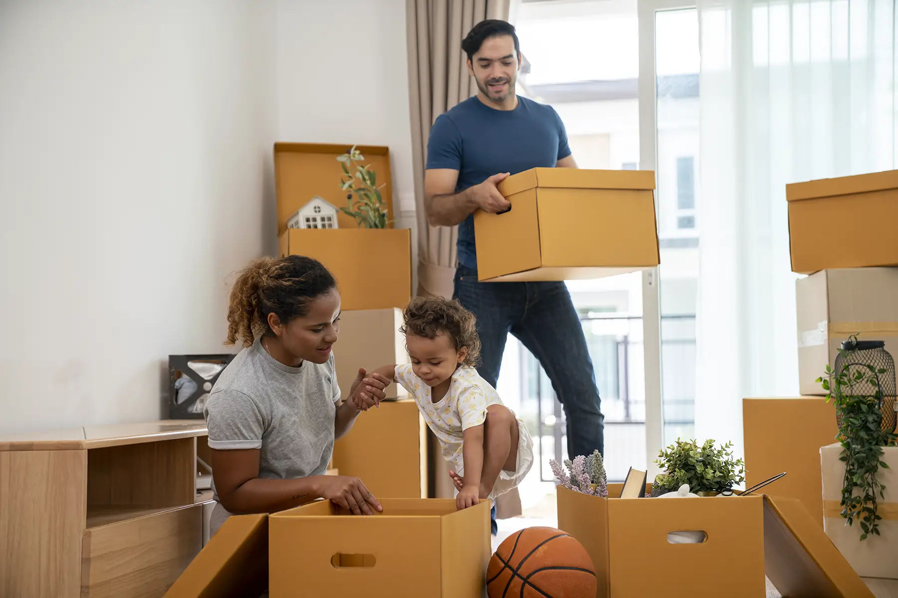 Parents playing with a small child in their new apartment full of moving boxes