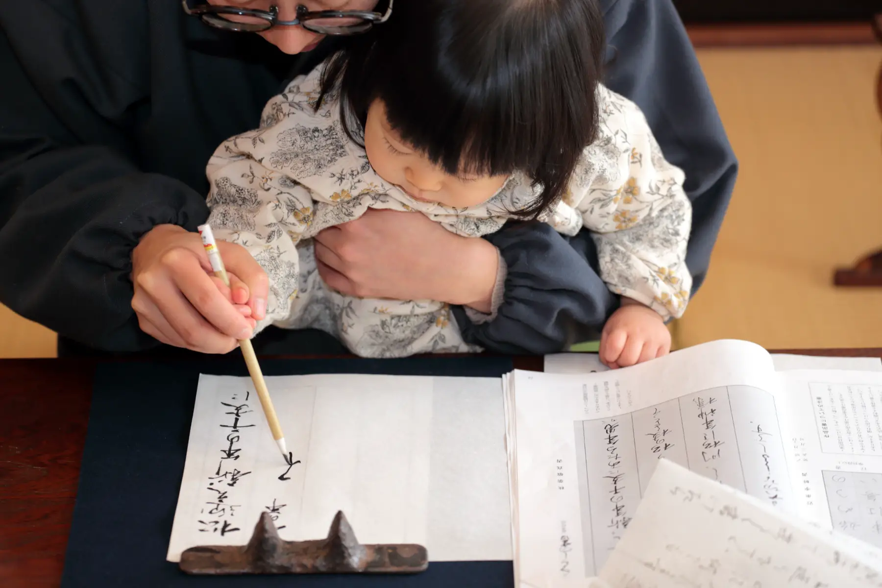 Father holds child and guides their hand to write kanji characters