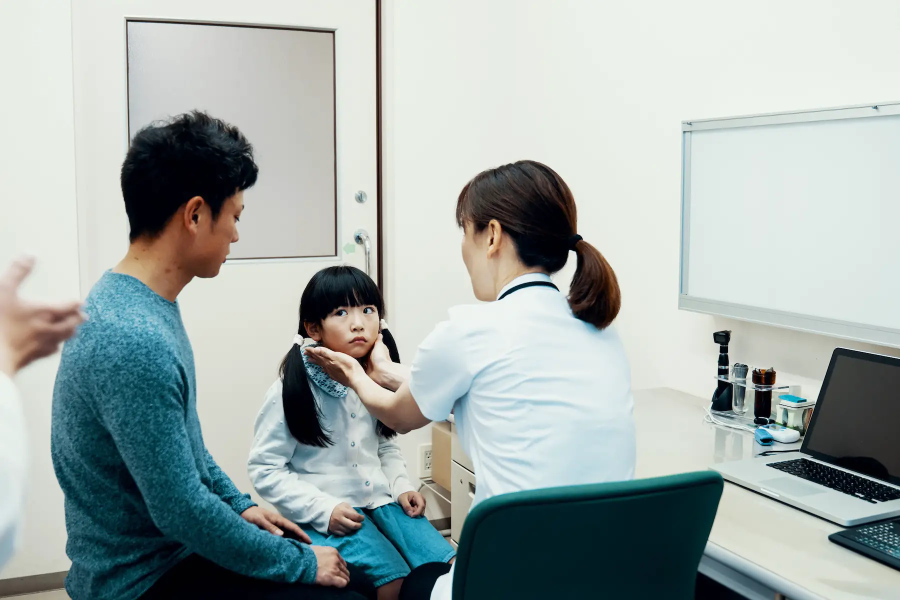 Mid adult father takes his young daughter to consult with a mature female doctor in a medical examination room at a doctor's office