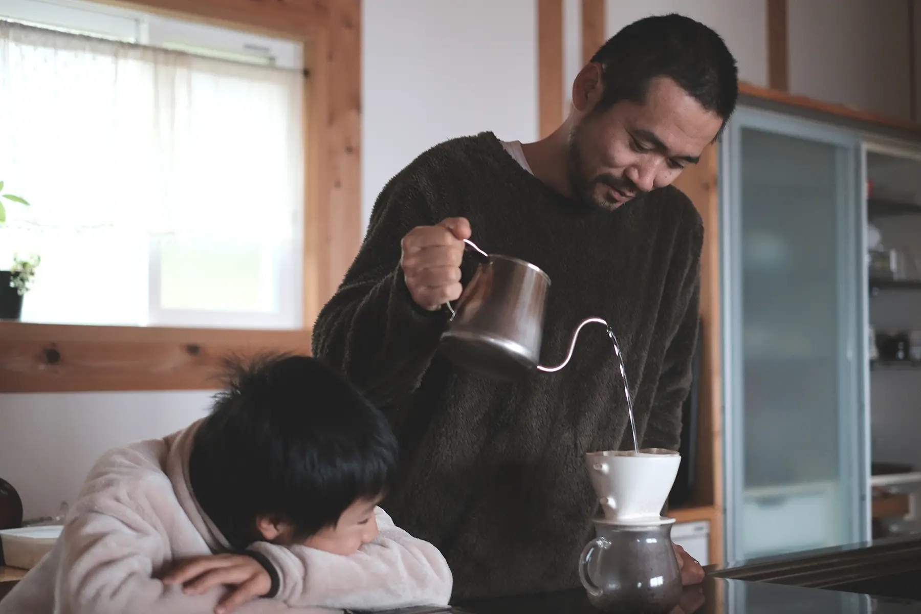 Boy looking at his father drip brewed coffee in kitchen in Japan