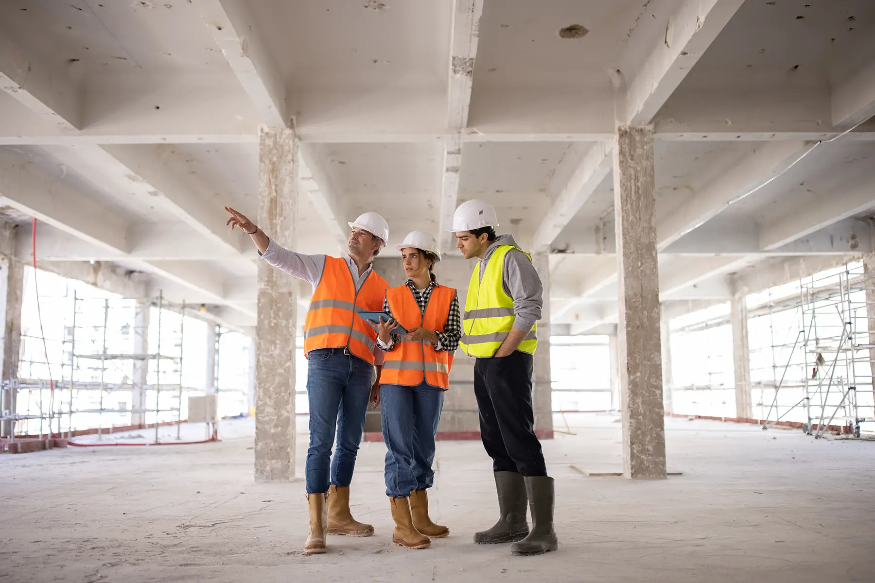 Three investors in hi-vis vests and hard hats looking at blueprints on a building site