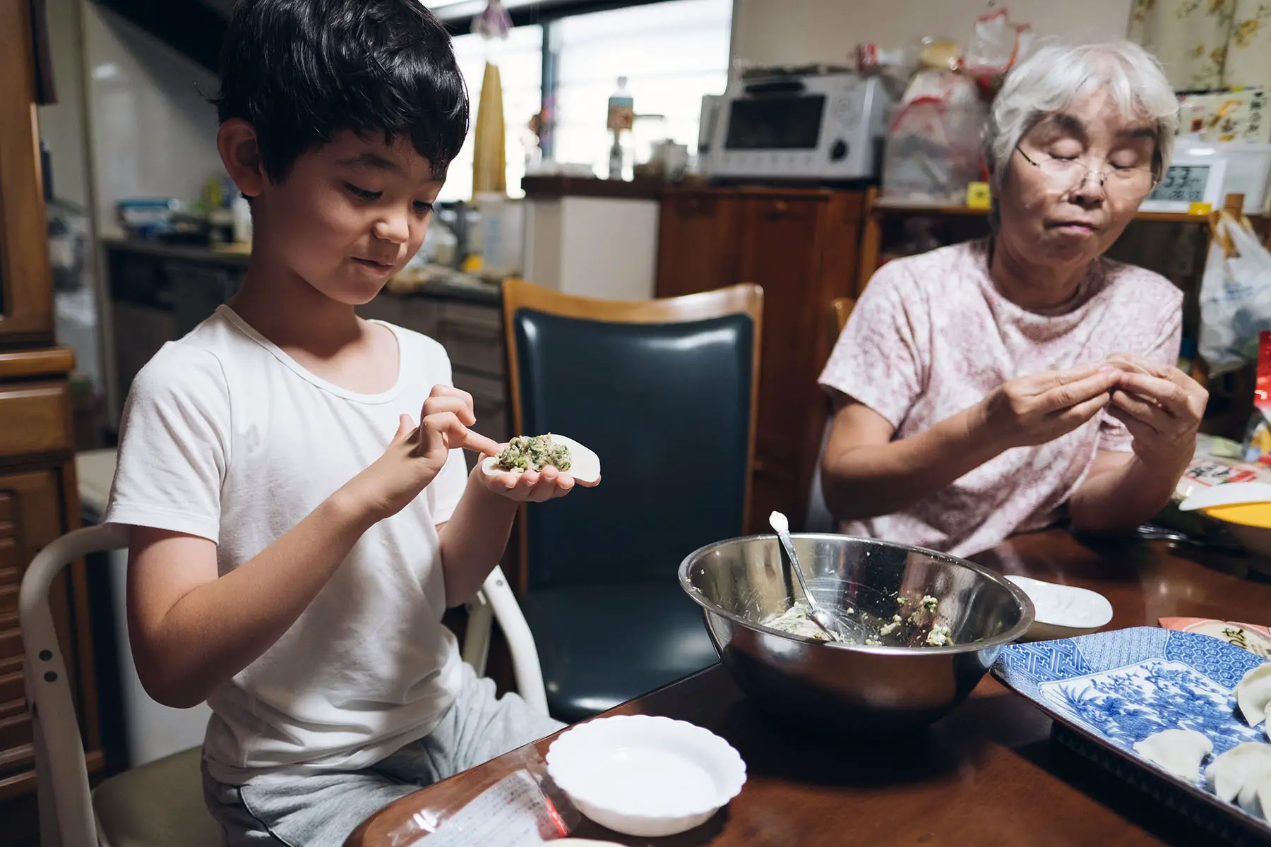 Grandson is helping his grandmother to prepare Japanese gyoza dumplings in the kitchen.