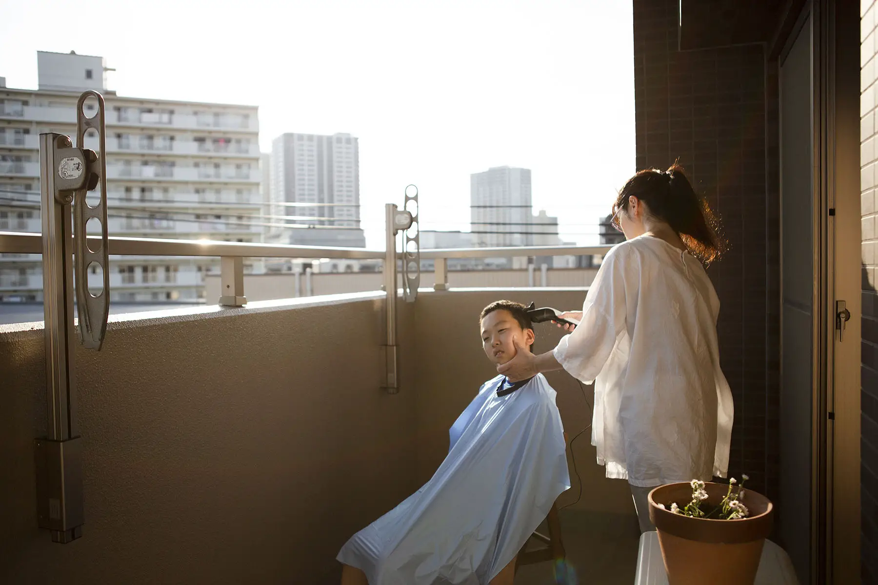 A woman is cutting her son's hair with a buzz cutter on a balcony in Saitama, Japan.