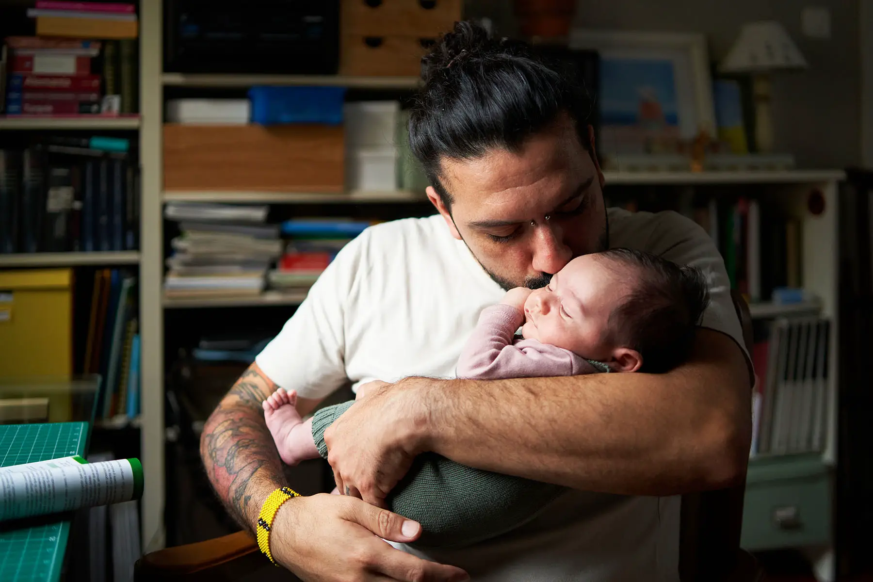 Tattooed father holding his baby in his arms while kissing its cheek.