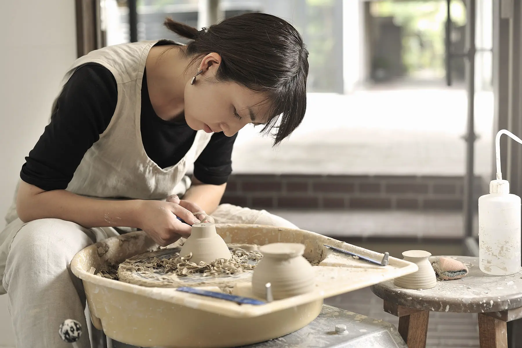 A Japanese woman is bent over a pottery wheel working on a new project