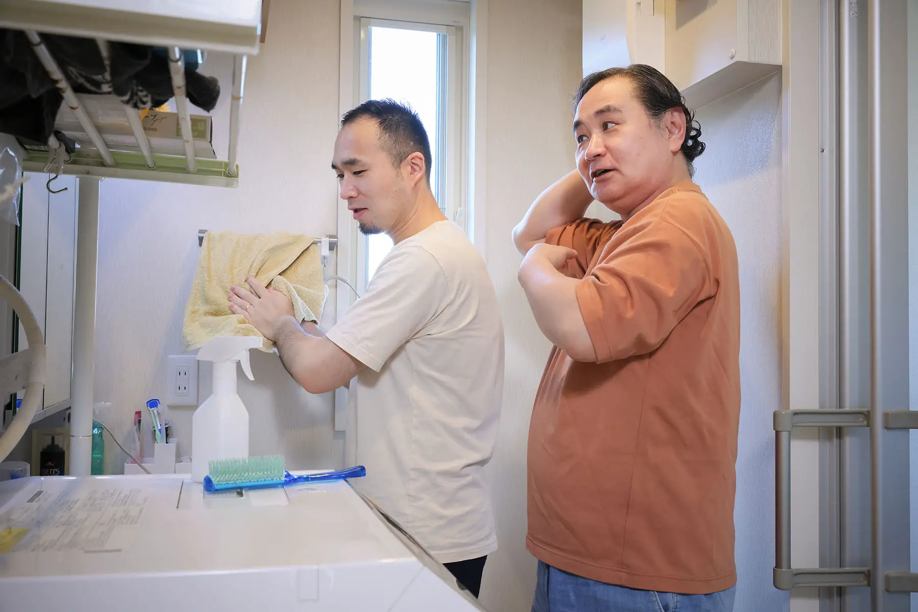 A couple doing their morning bathroom routine. One person is drying his hands, the other is checking his hair.