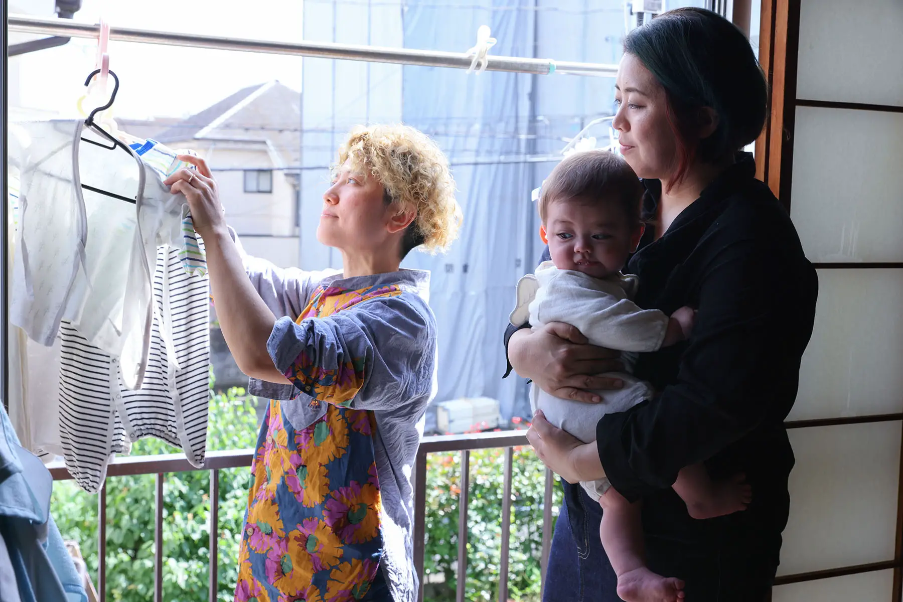 LGBTQ couple hanging laundry on the balcony, one is holding a baby.