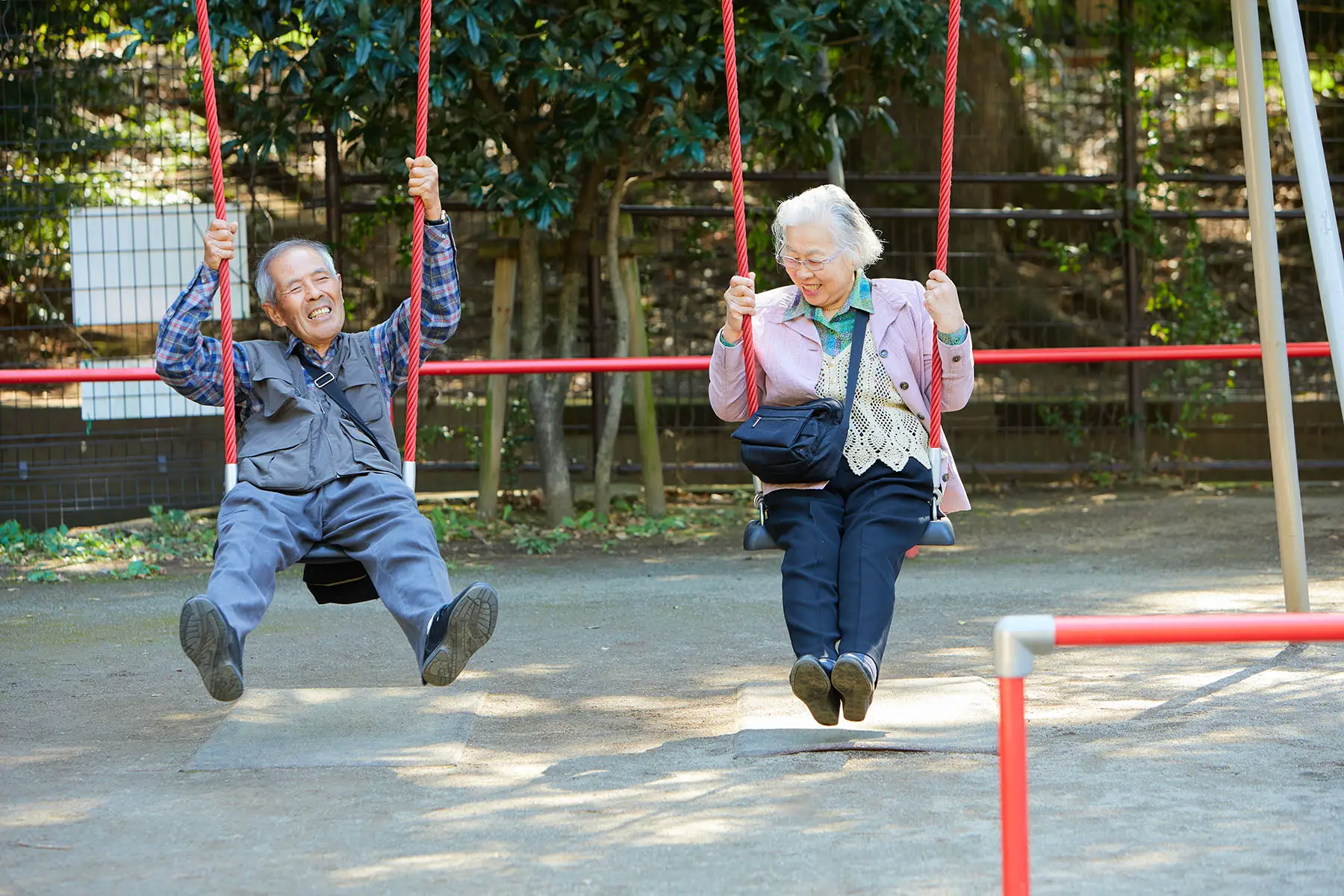 Elderly couple laughing while theyre on a set of swings.