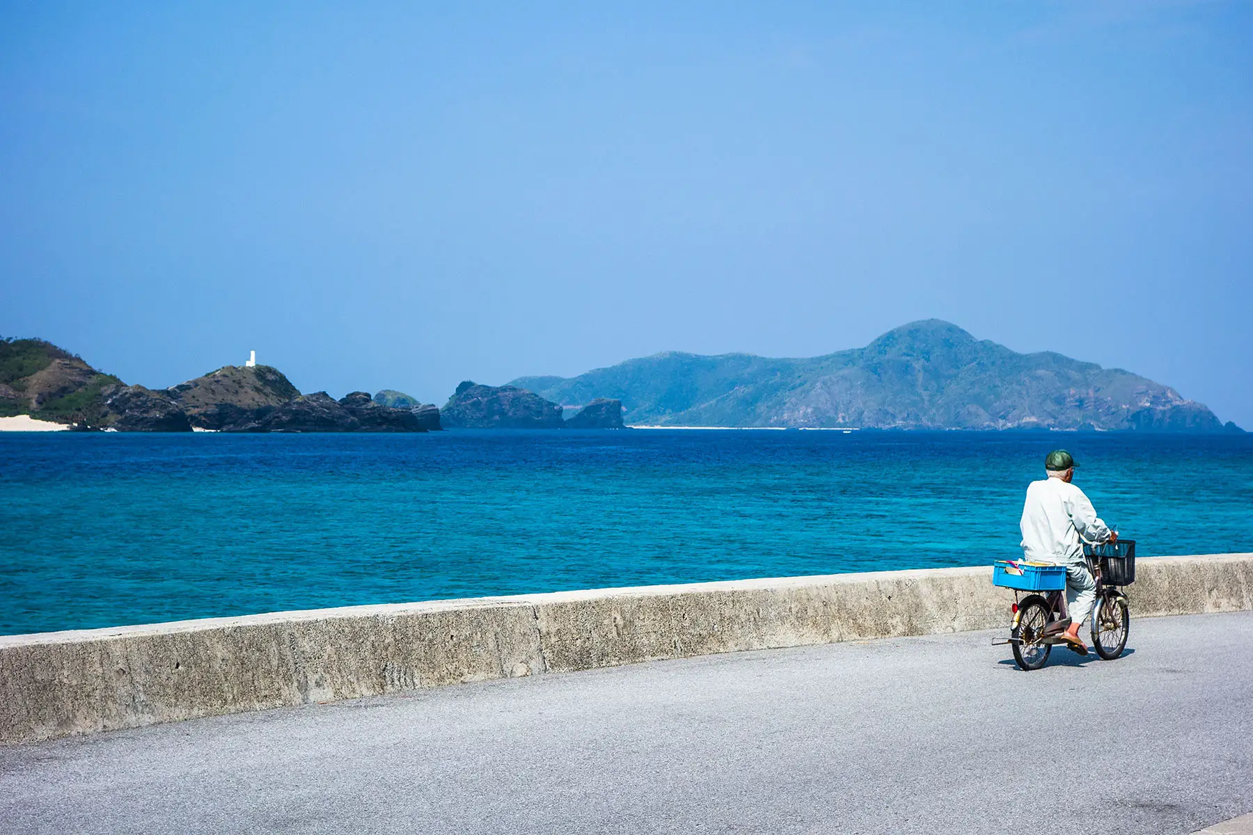 Old man on a bike cycling near the beach front on Okinawa island.