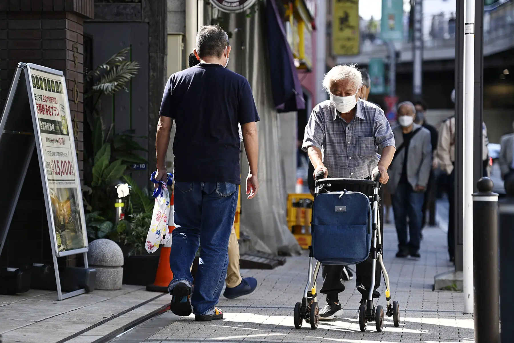Old man walking on the streets of Japan with a walker.