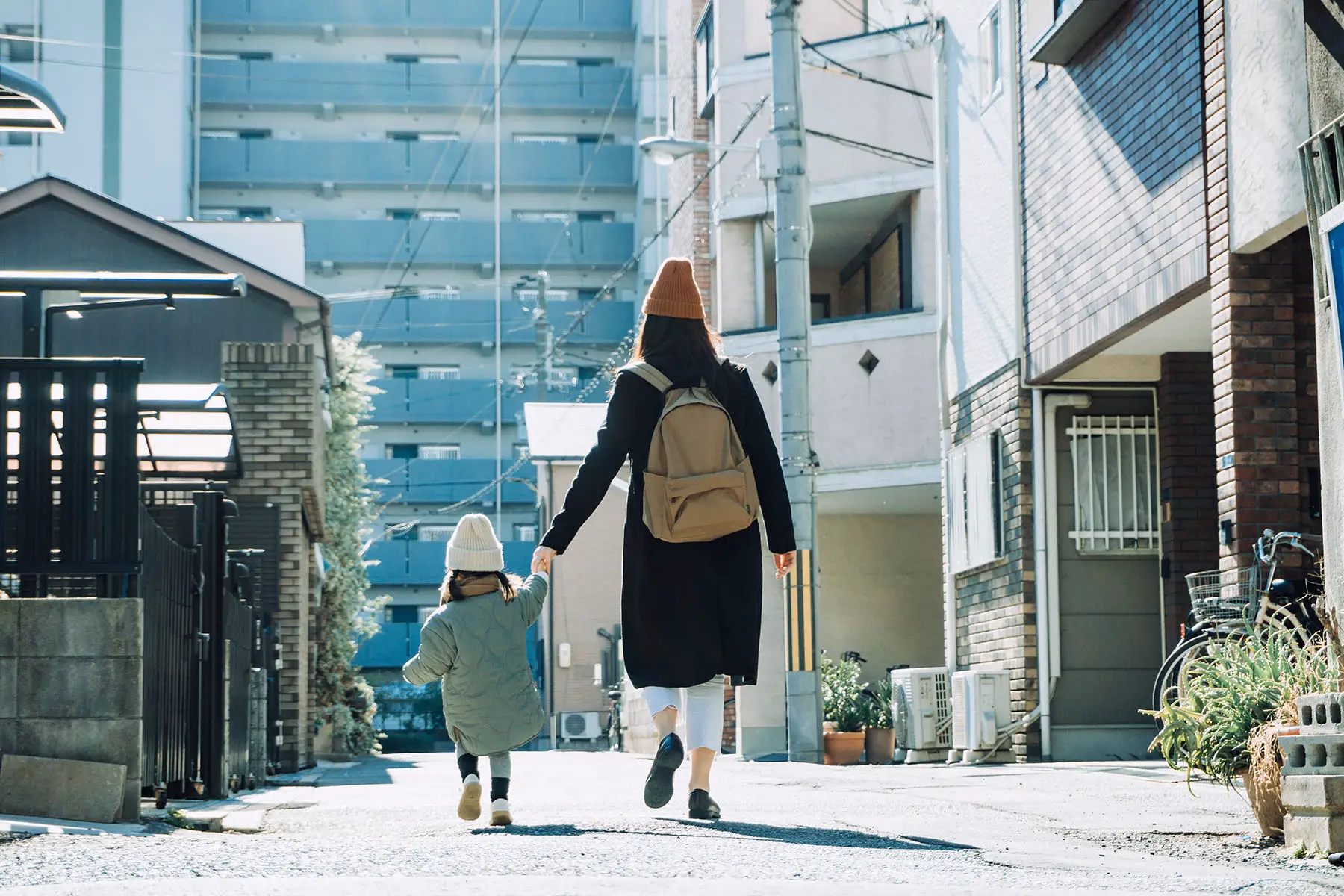 Mother holding hands with little daughter as they walk along a local city street in Osaka (Japan) on a sunny winter's day.