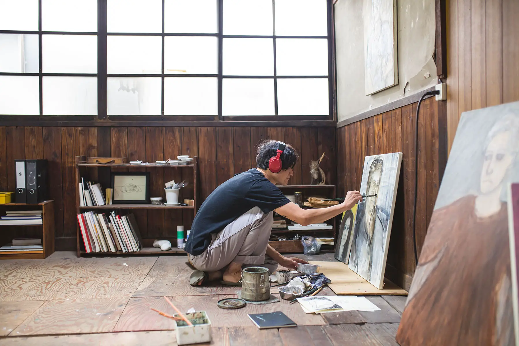 Man sitting on the floor painting with oil paint in his studio, listening to something on his headphones.