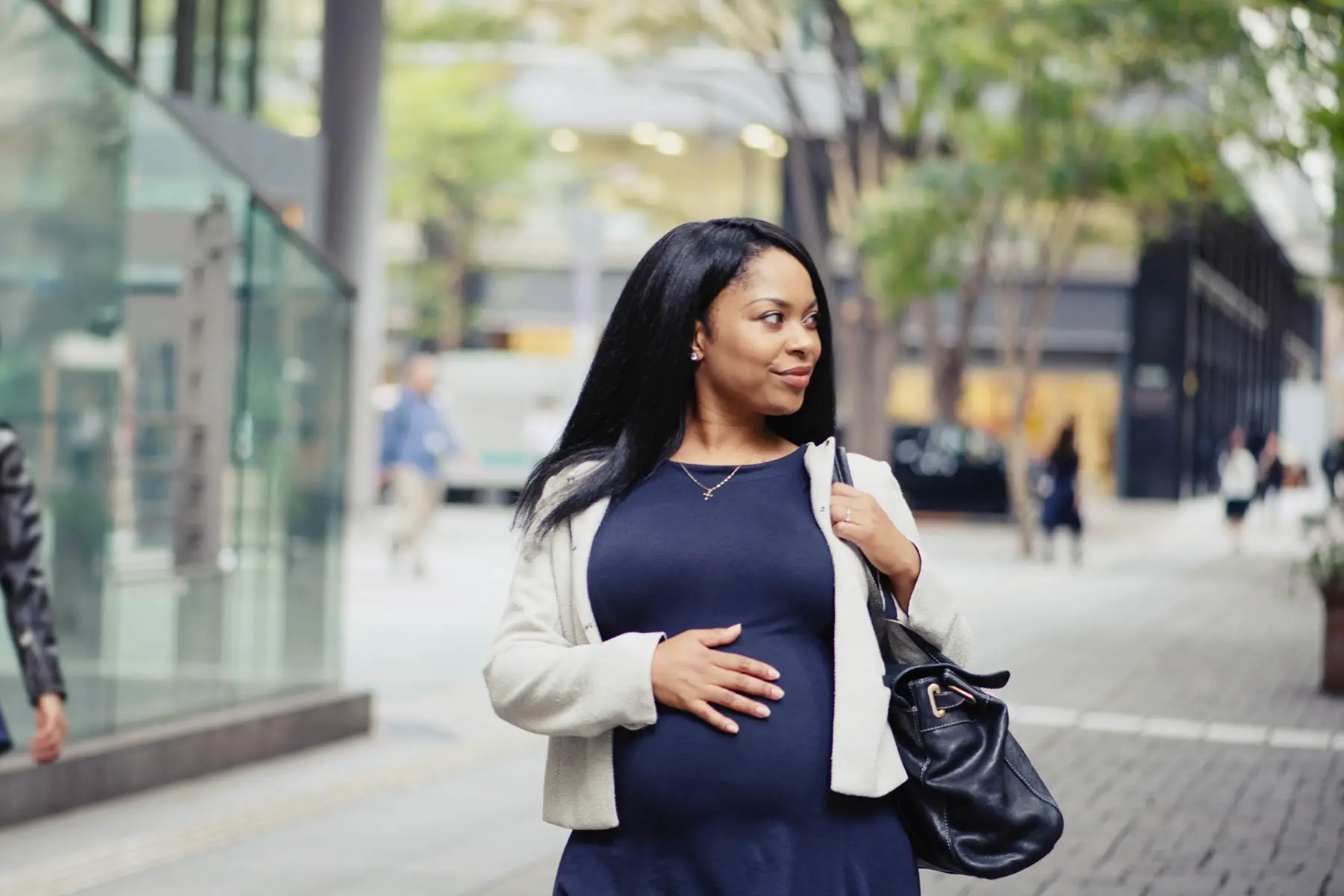 Pregnant woman looking gorgeous while strutting downtown with one hand on her belly.