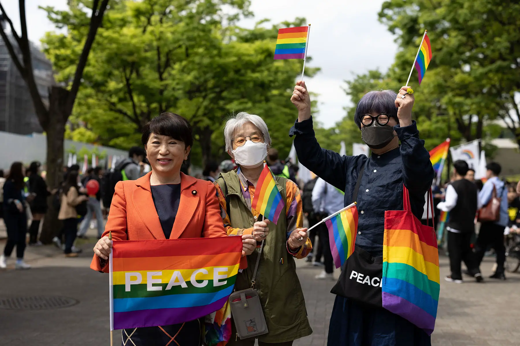 Three mature ladies are smiling and waving rainbow flags during the 2023 Tokyo Rainbow Parade in Tokyo, Japan