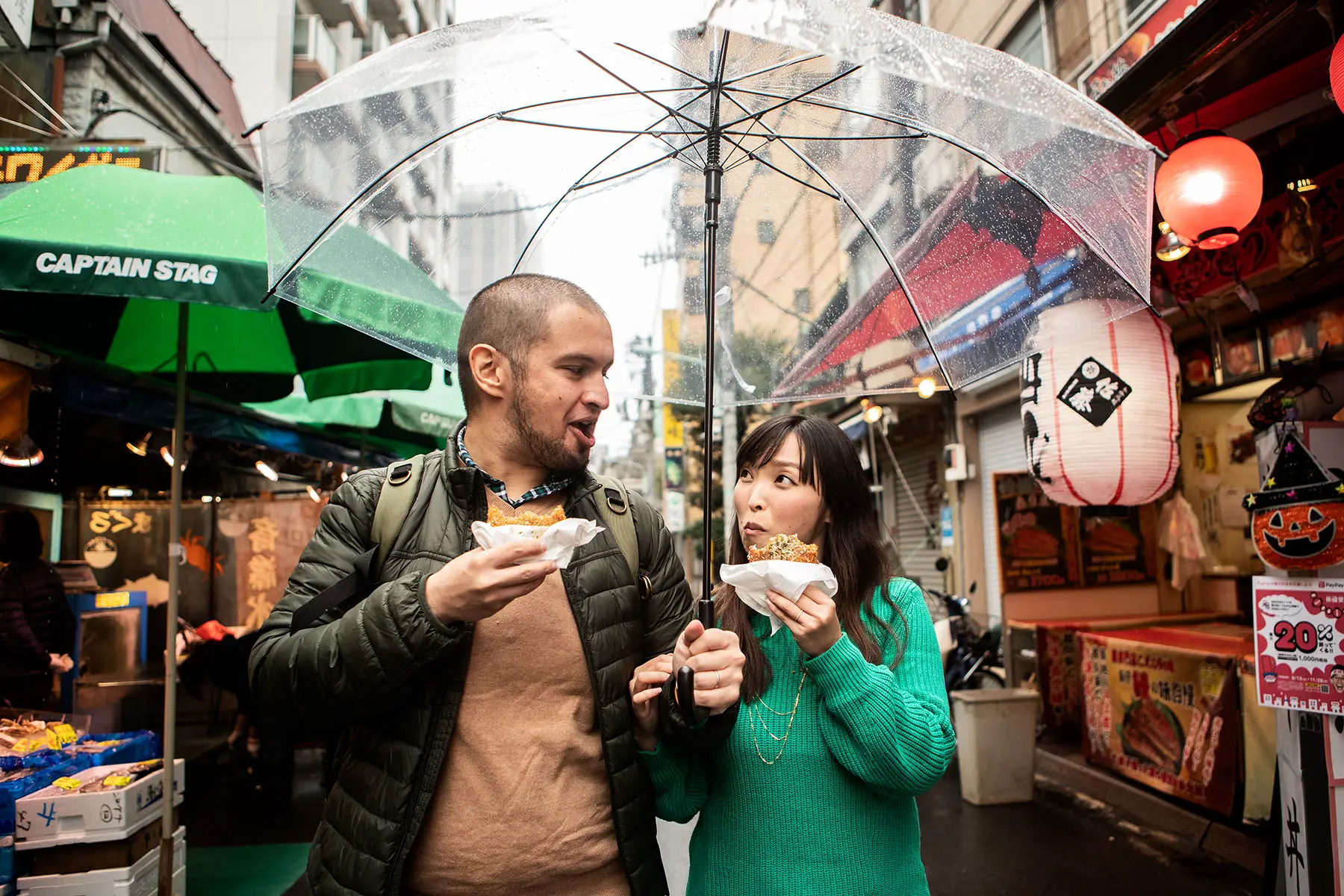 A couple walking in the rain, holding an umbrella, and eating street food in Tokyo, Japan.