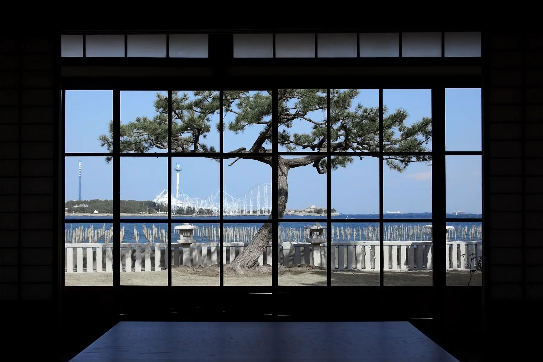 Japanese looking window showing a tree and the seaside.