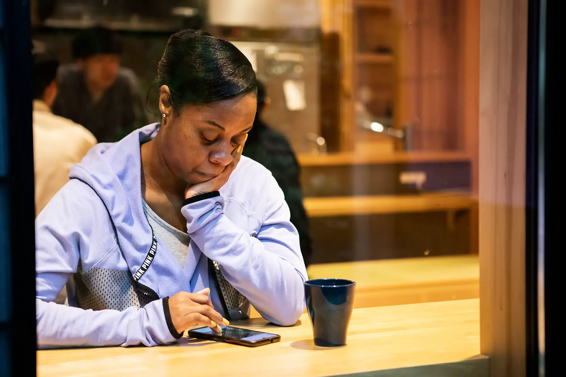 Woman looking down at her phone while waiting at a coffee house.