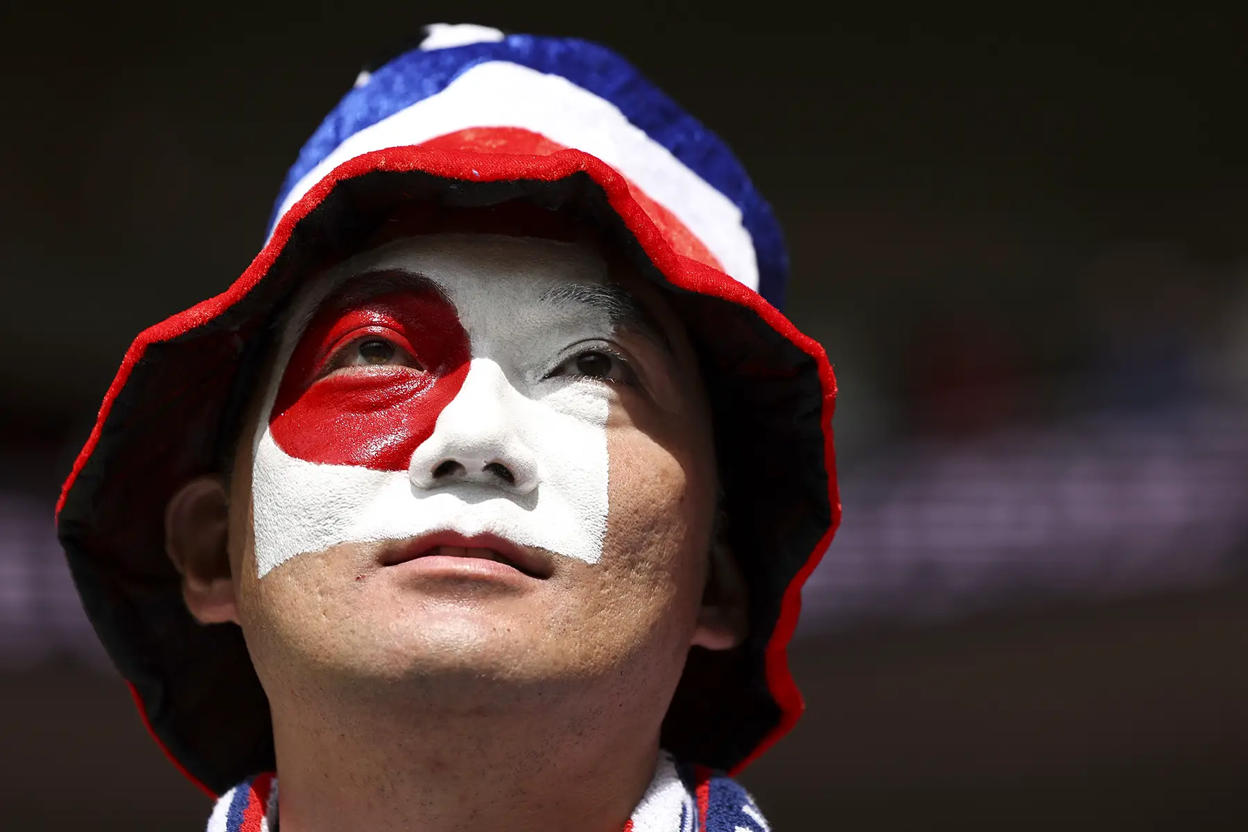 Man wearing a red, blue and red hat with a Japanese flag painted on his face