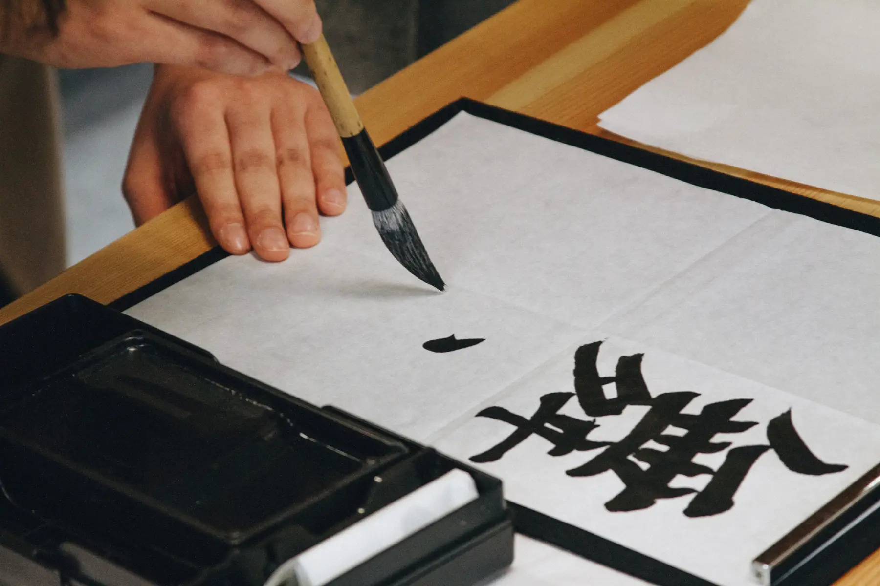 Person painting kanji on a sheet of paper