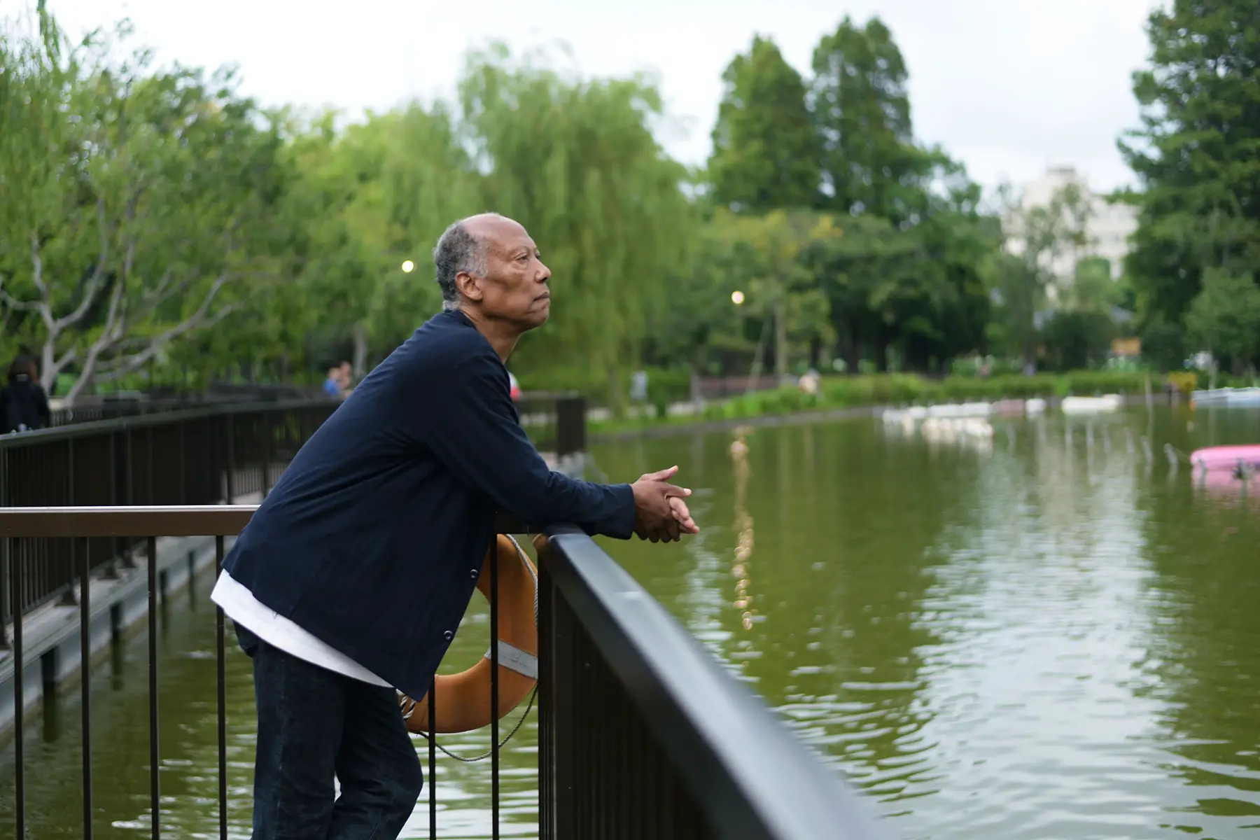 A senior man leaning on railings, looking at a lake.