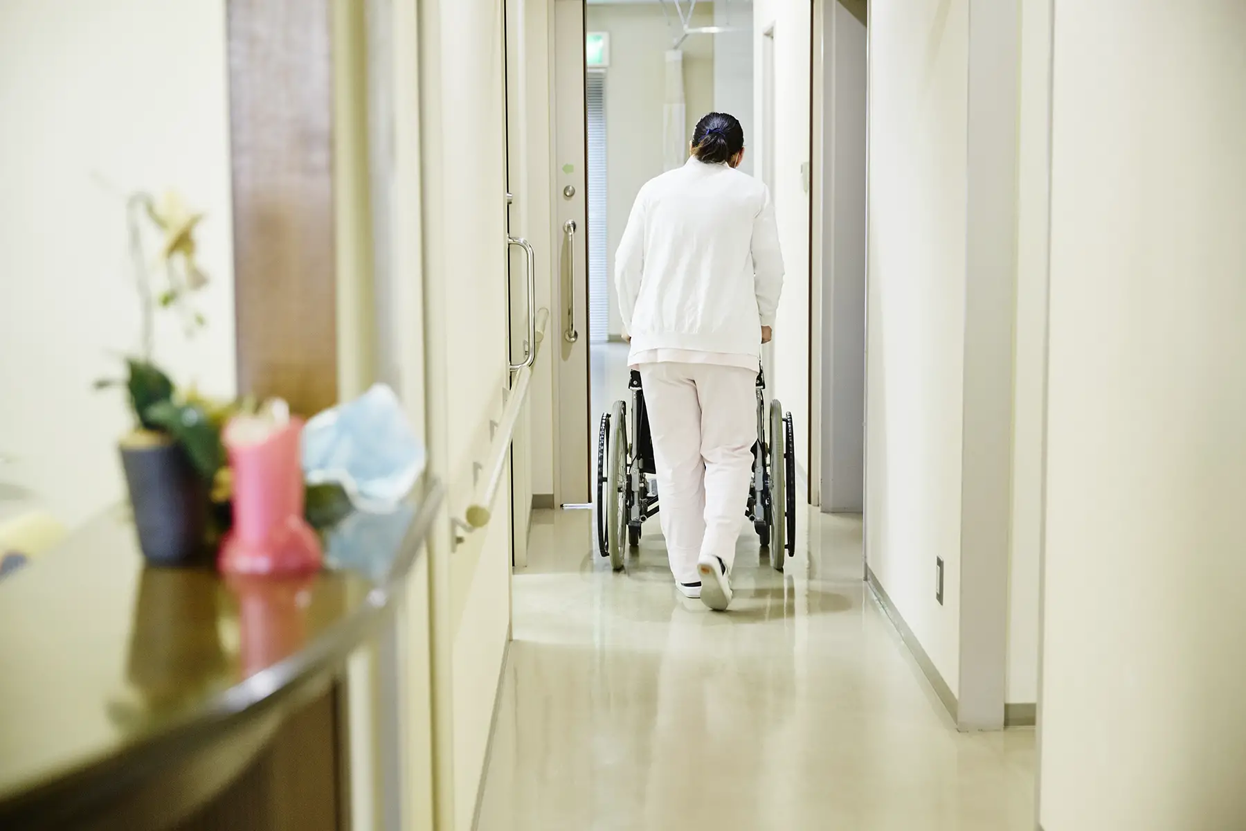 Nurse pushing a patient's wheelchair down the hall away from camera
