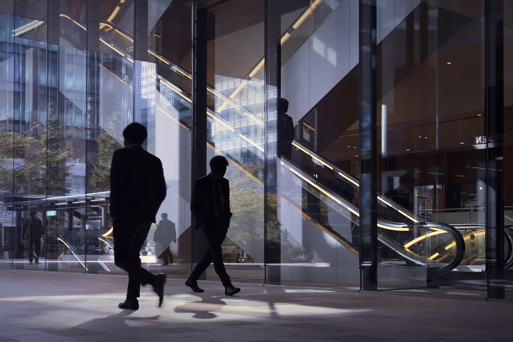 Silhouettes of office workers walking around in a office lobby with large windows and escalators