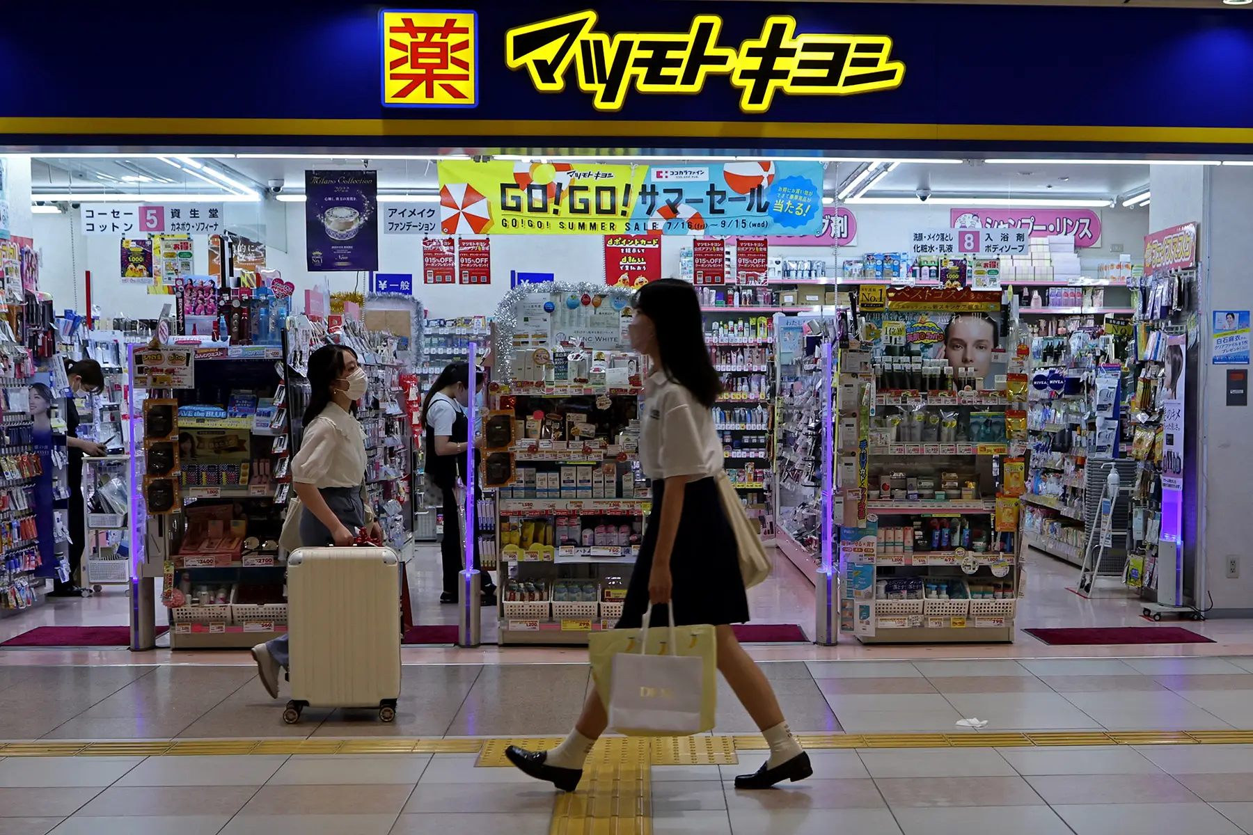 Two shoppers walk past a pharmacy in Kyoto, wearing masks