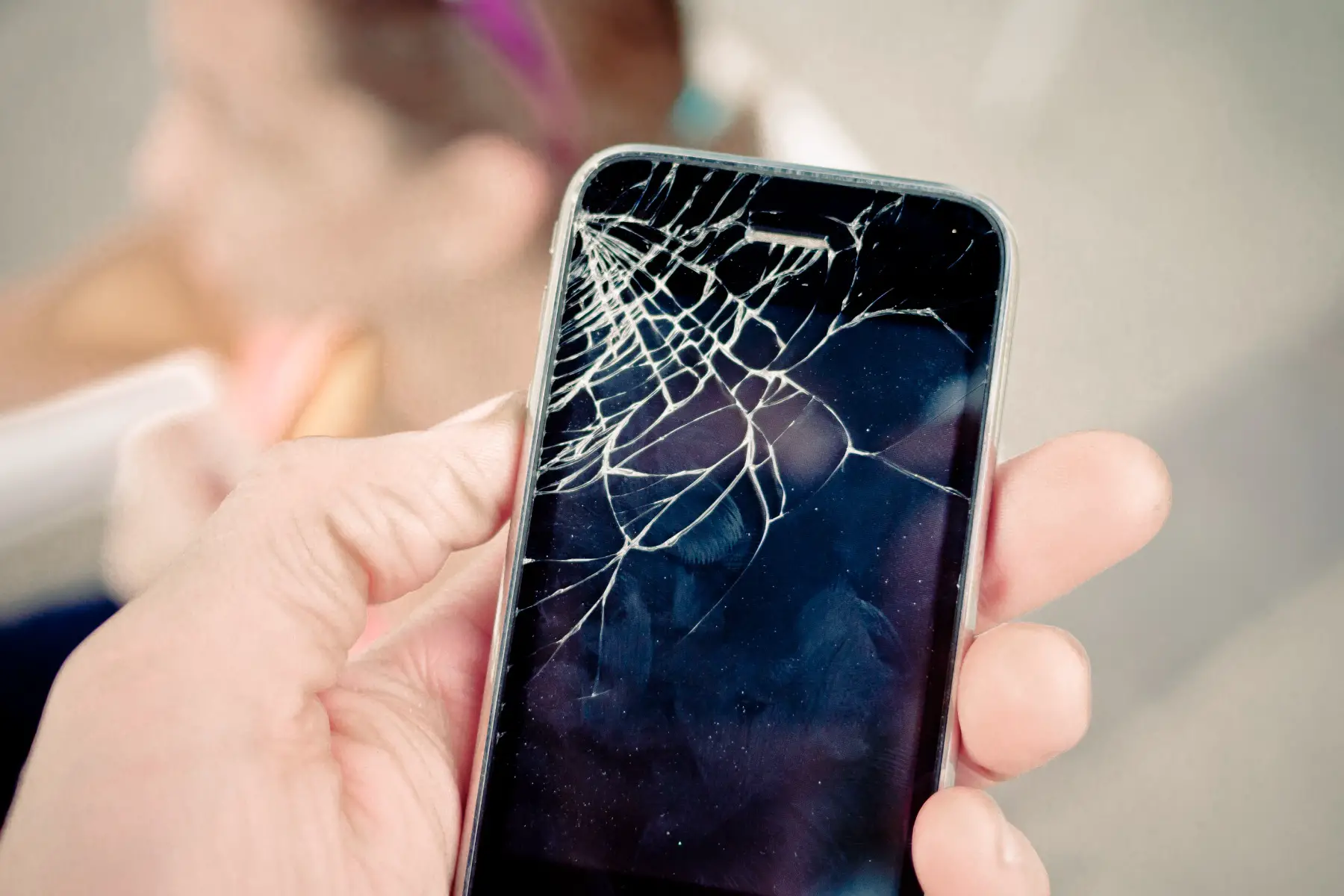 a close up of a hand holding a smartphone with a shattered screen