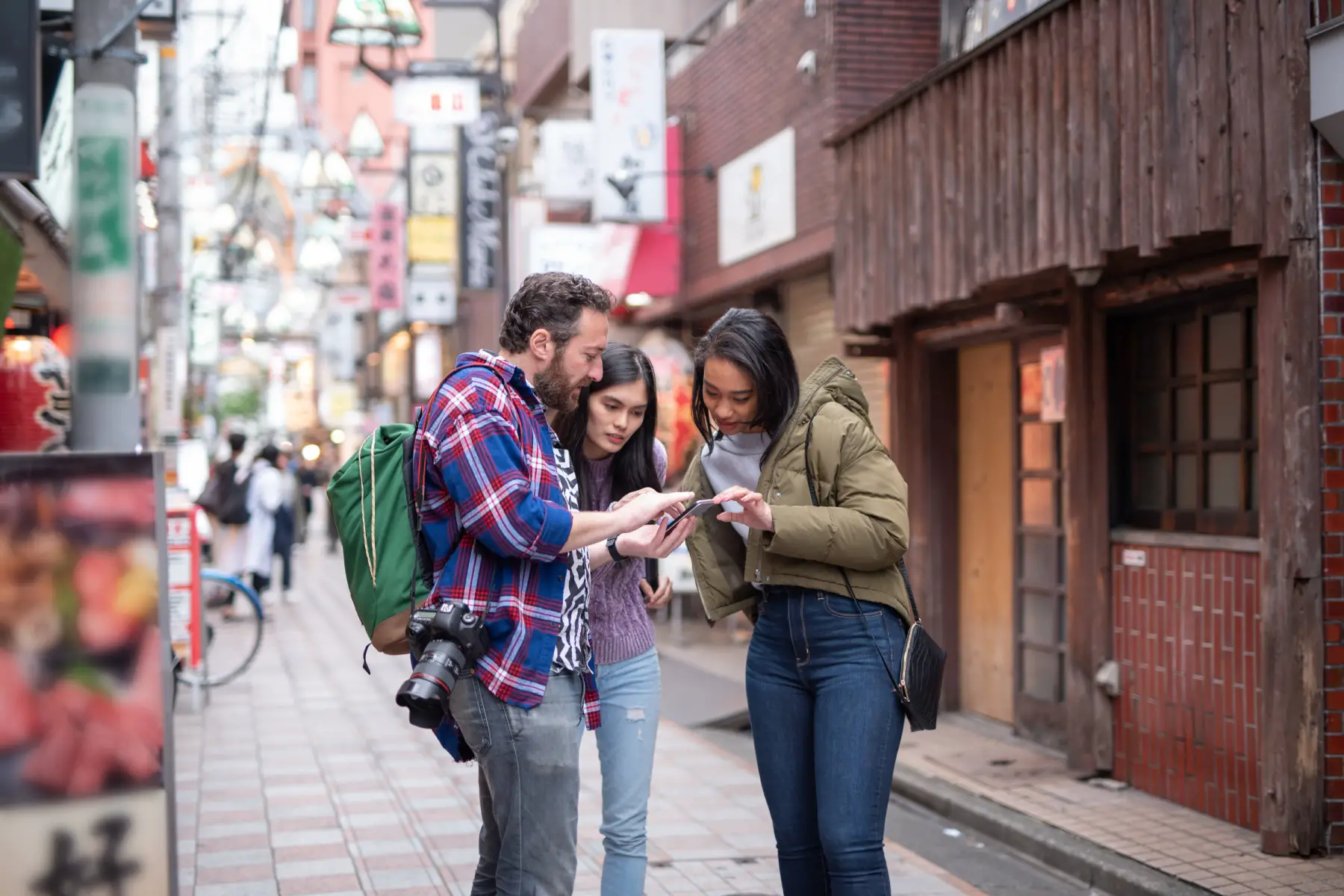 a tourist standing in a street in Tokyo and looking down at his phone with two woman as he asks for directions