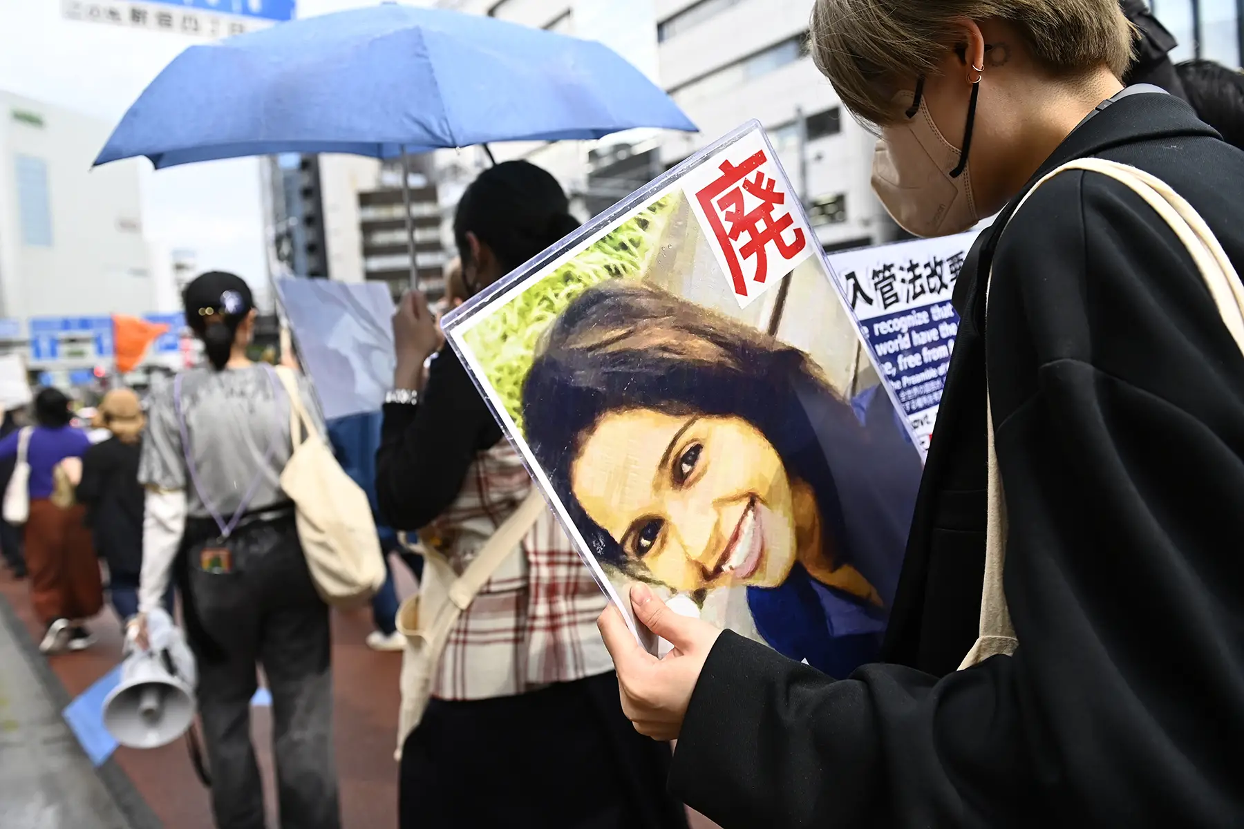 Closeup of the back of a woman holding a photograph at a protest. The photo shows a Sri Lankan woman, Rathnayake Lianage Wishma Sandamali.