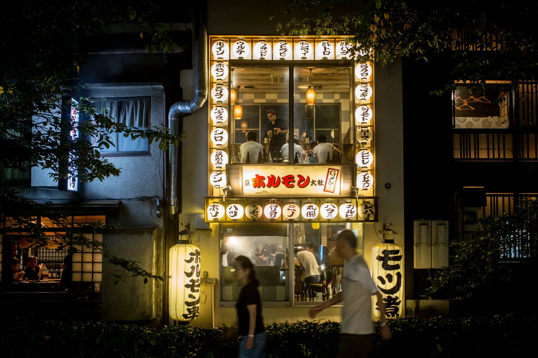 An illuminated two-floor restaurant operating at night in Kyoto