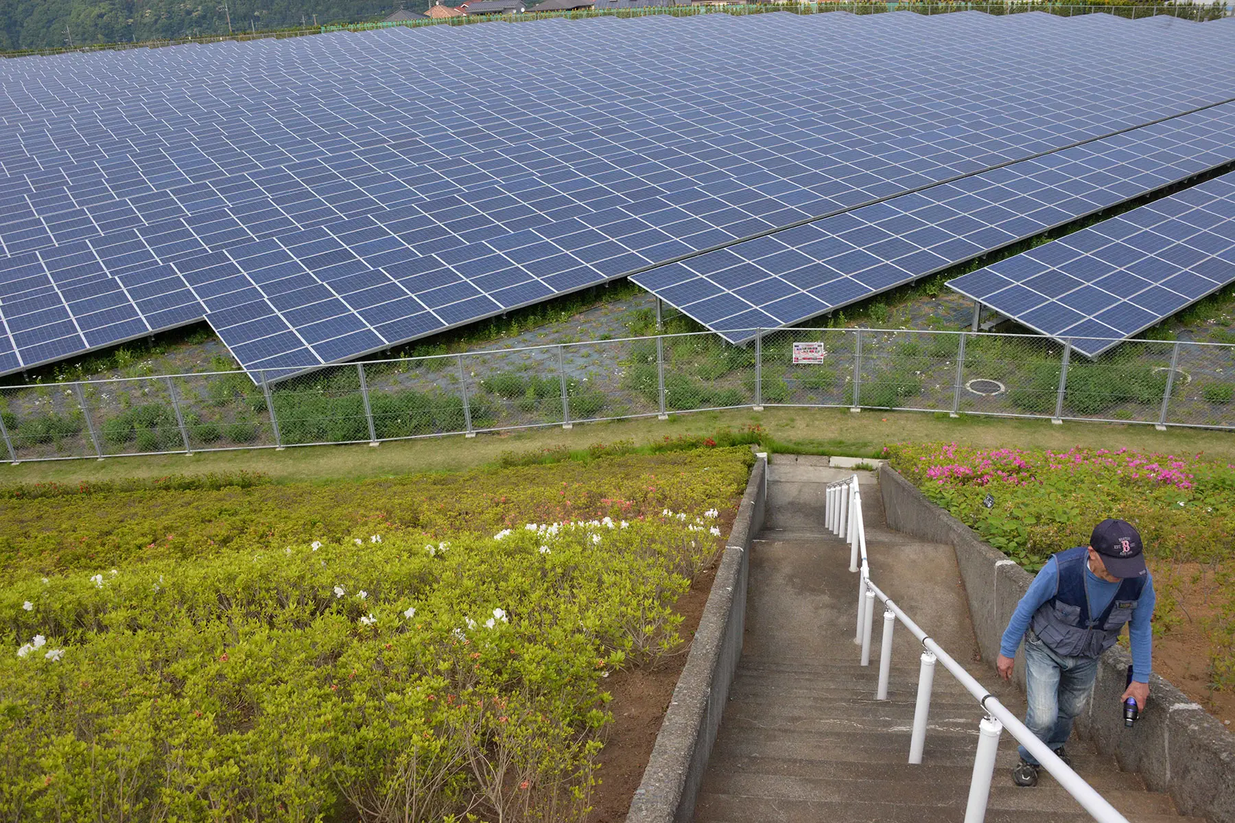 A man walks up the stairs, behind him the Aikawa Solar Power Plant - green utilities in Japan