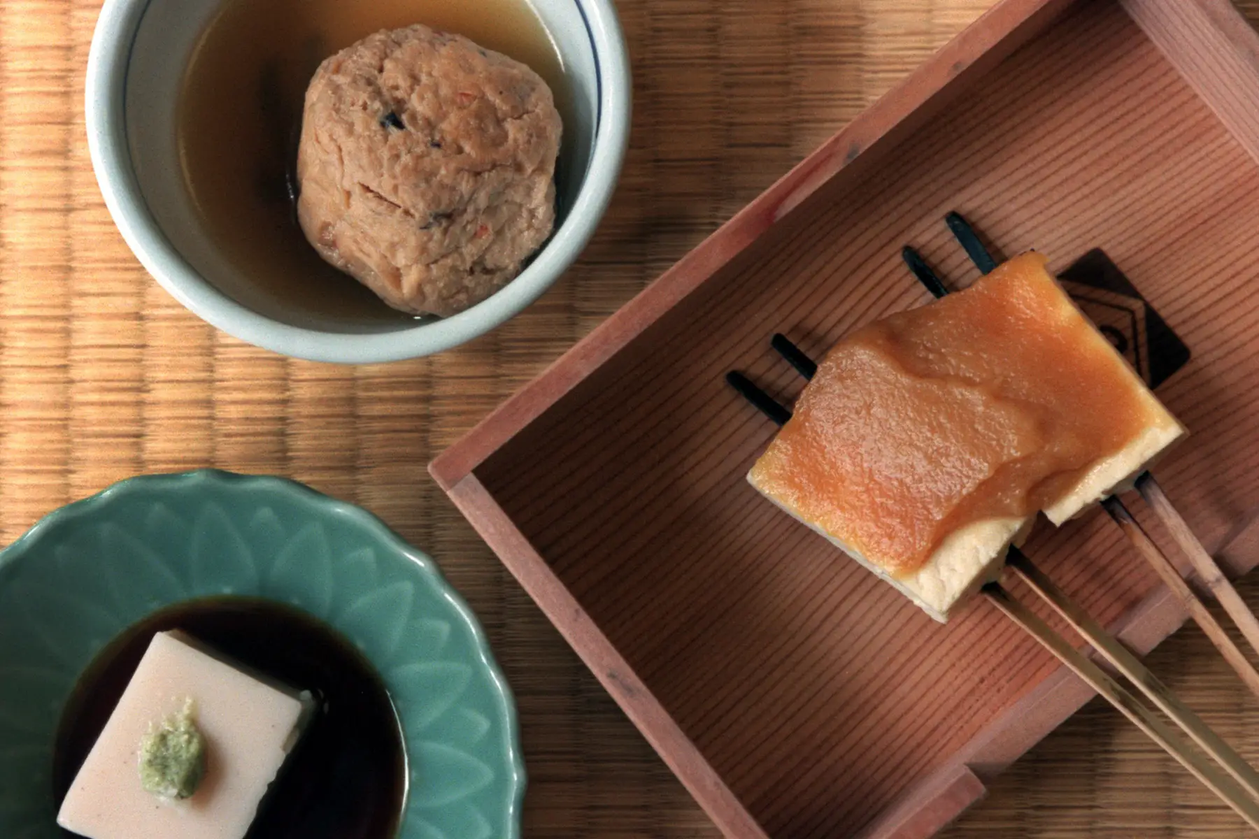 A selection of soy-based dishes: tofu dumpling, tofu, soy sauce, and tofu served on chopsticks with miso paste