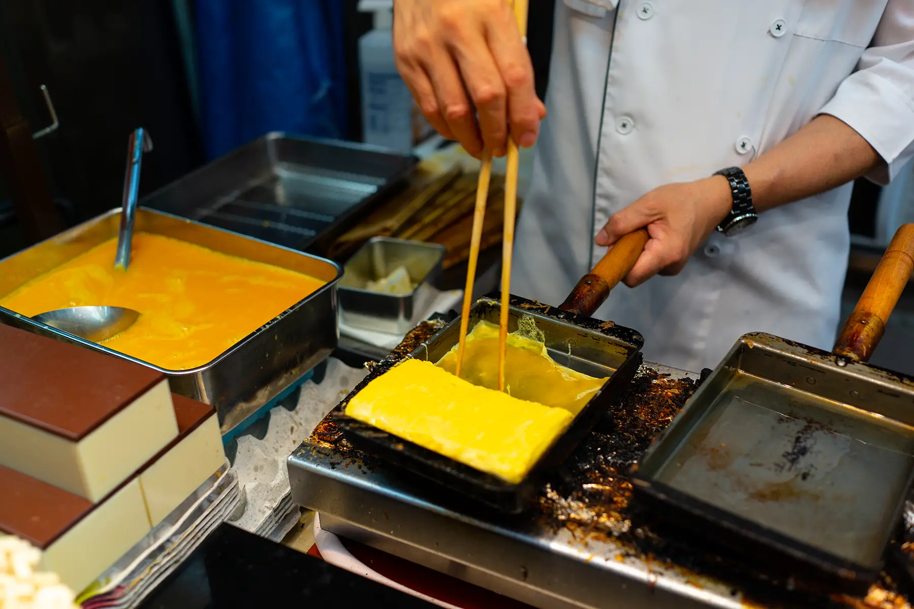 A chef cooking tamagoyaki, an egg dish which they are making in a square pan