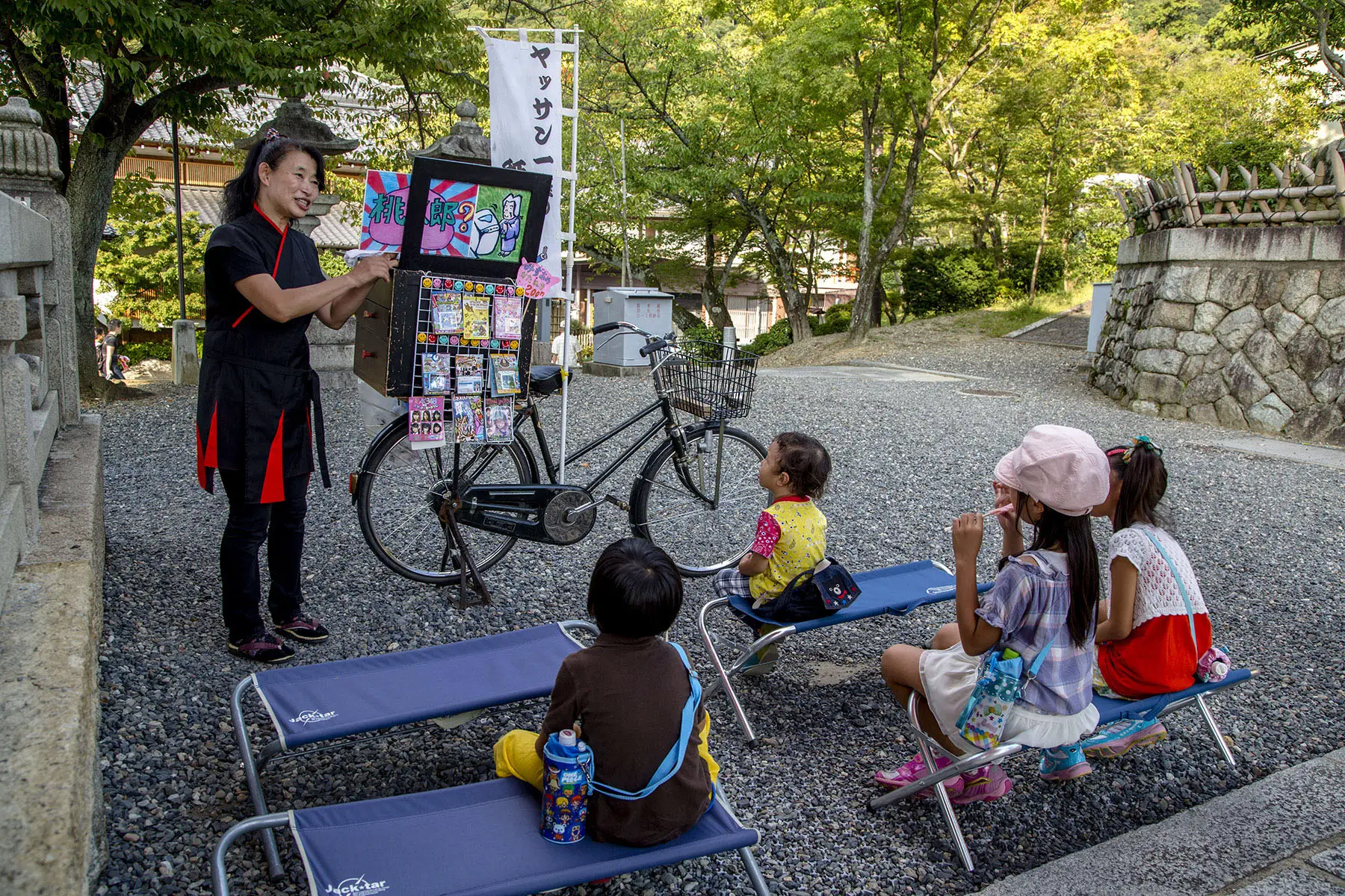A teacher telling a famous Japanese story Momotaro by playing traditional Kami-shibai for kids in a park in Kyoto