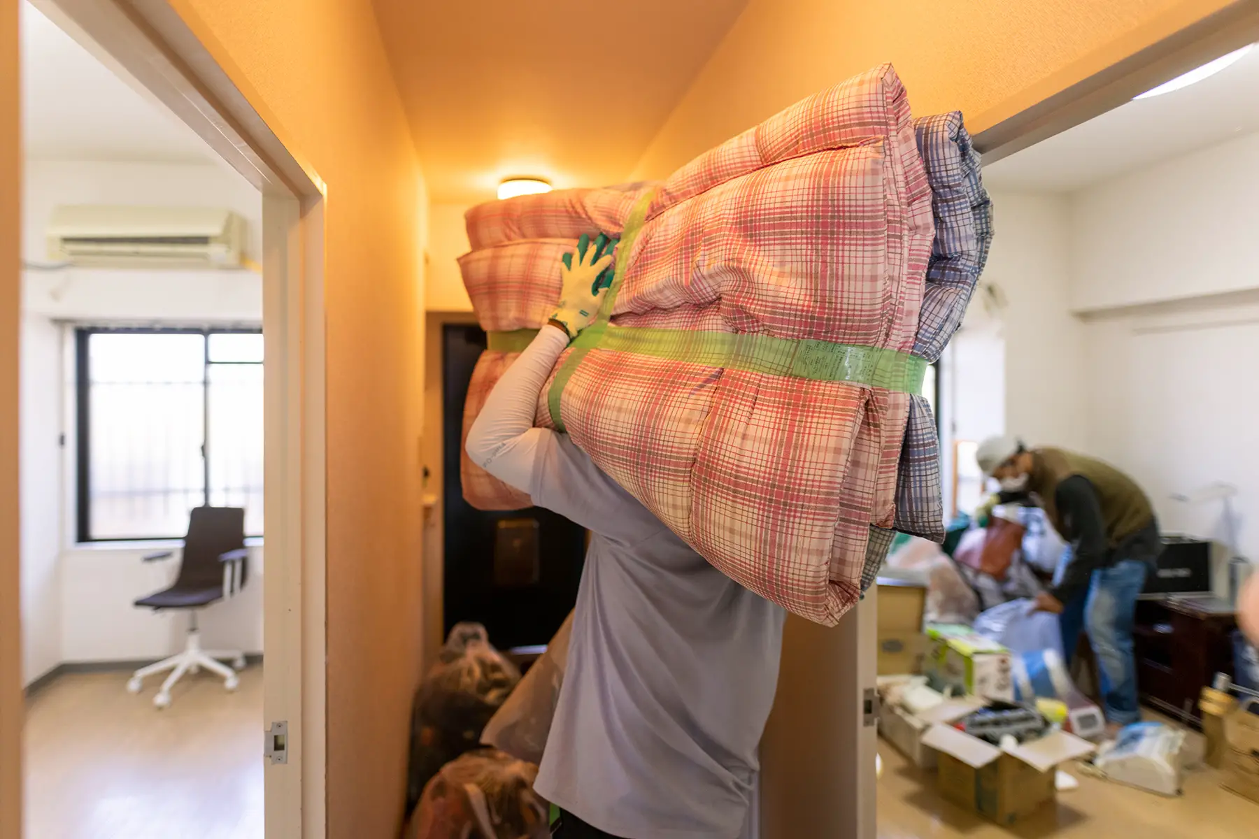 A family unpack in their new apartment, a person is carrying a couple of folded up futon mattresses