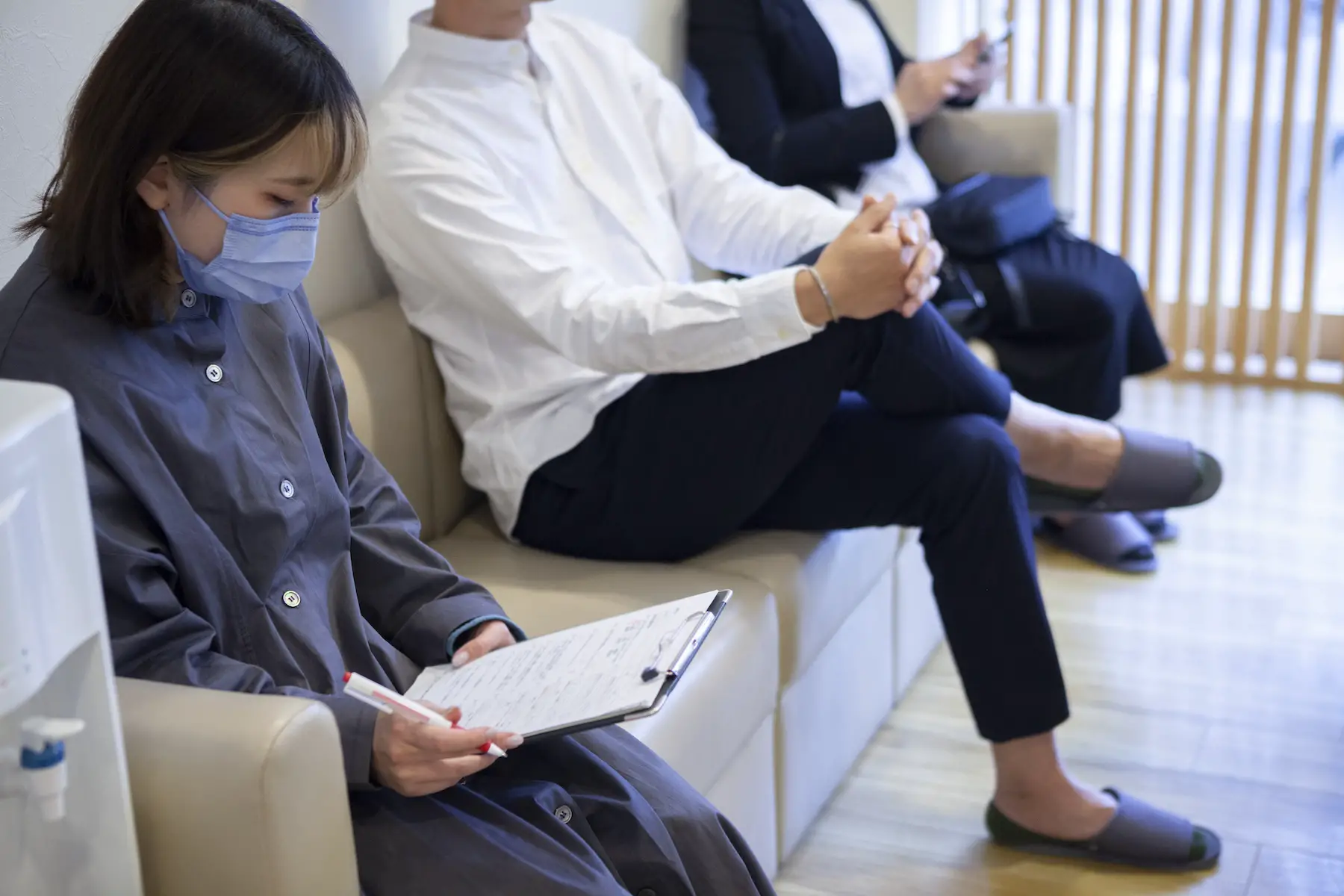 A patient waits to be seen at a clinic while wearing a mask and filling out medical forms