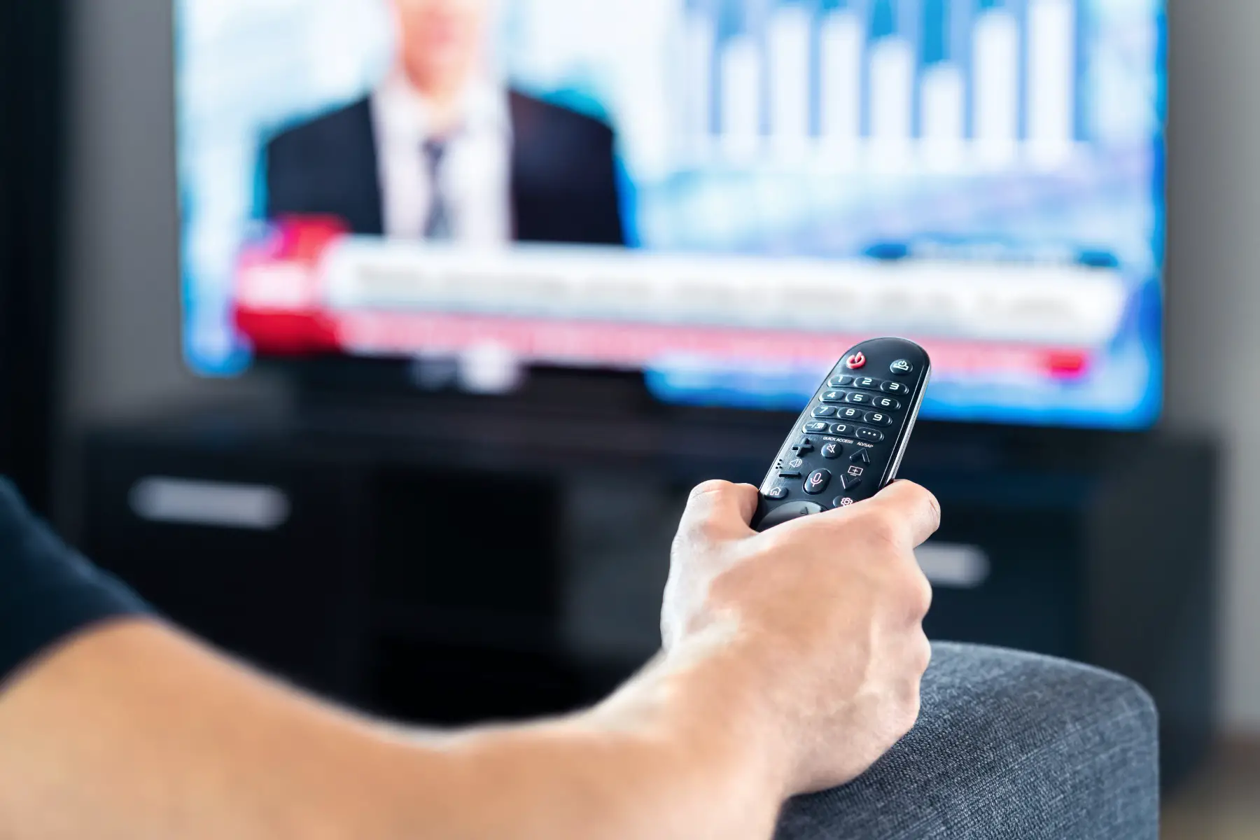 close up of a man's arm with his hand holding a remote as he watches television at home