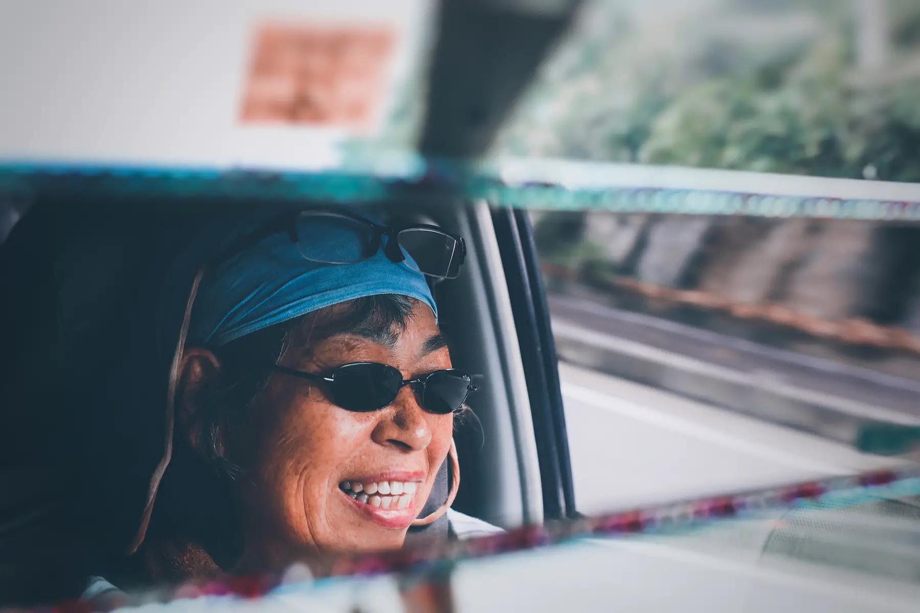 The reflection of a woman smiling in her rearview mirror while driving