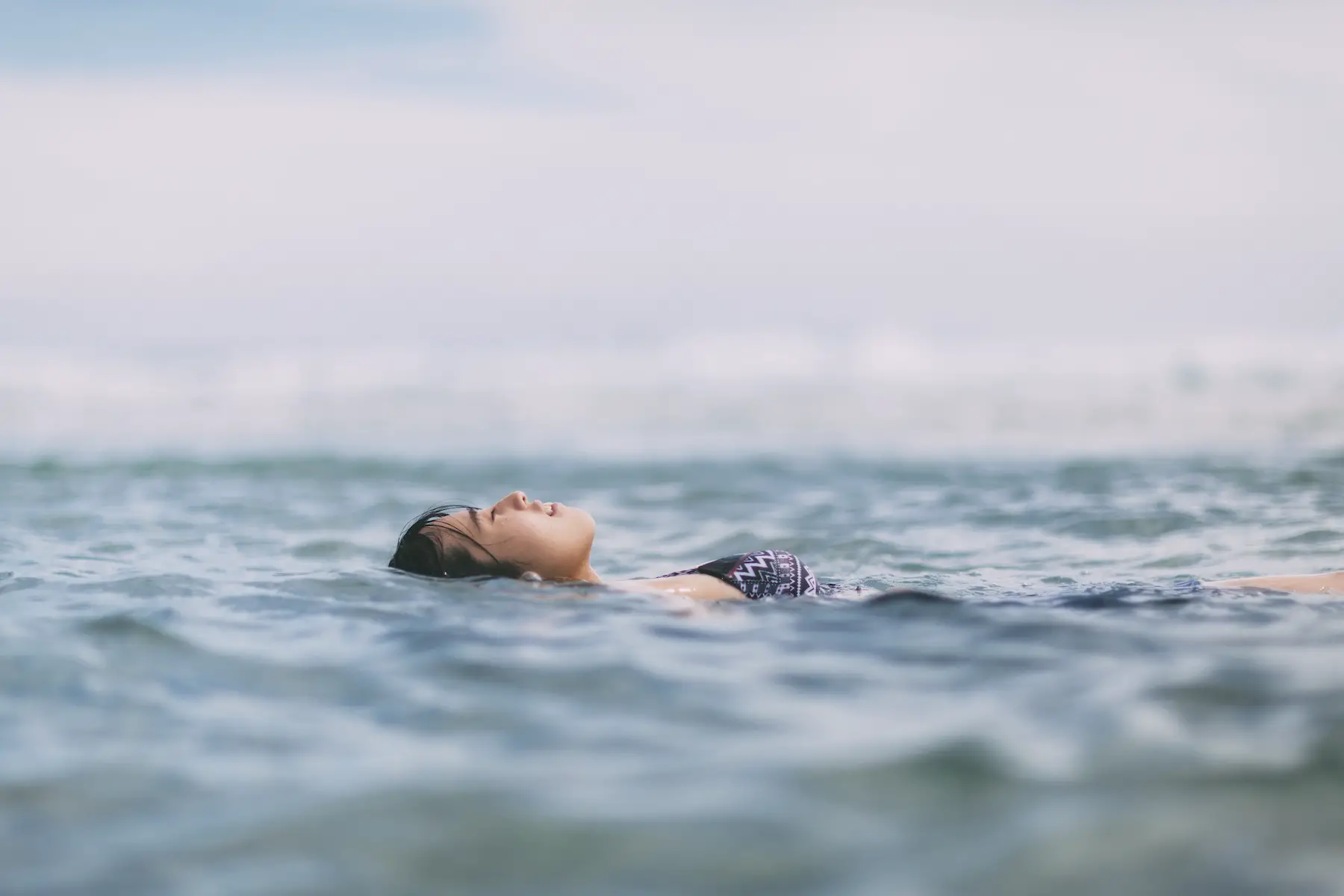 Side view of a young woman floating on her back in the sea with her eyes closed on a cloudy day