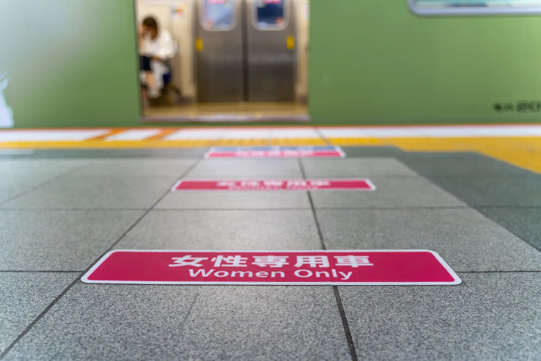 Rectangular pink signs on the ground of a train platform in Osaka, Japan read 