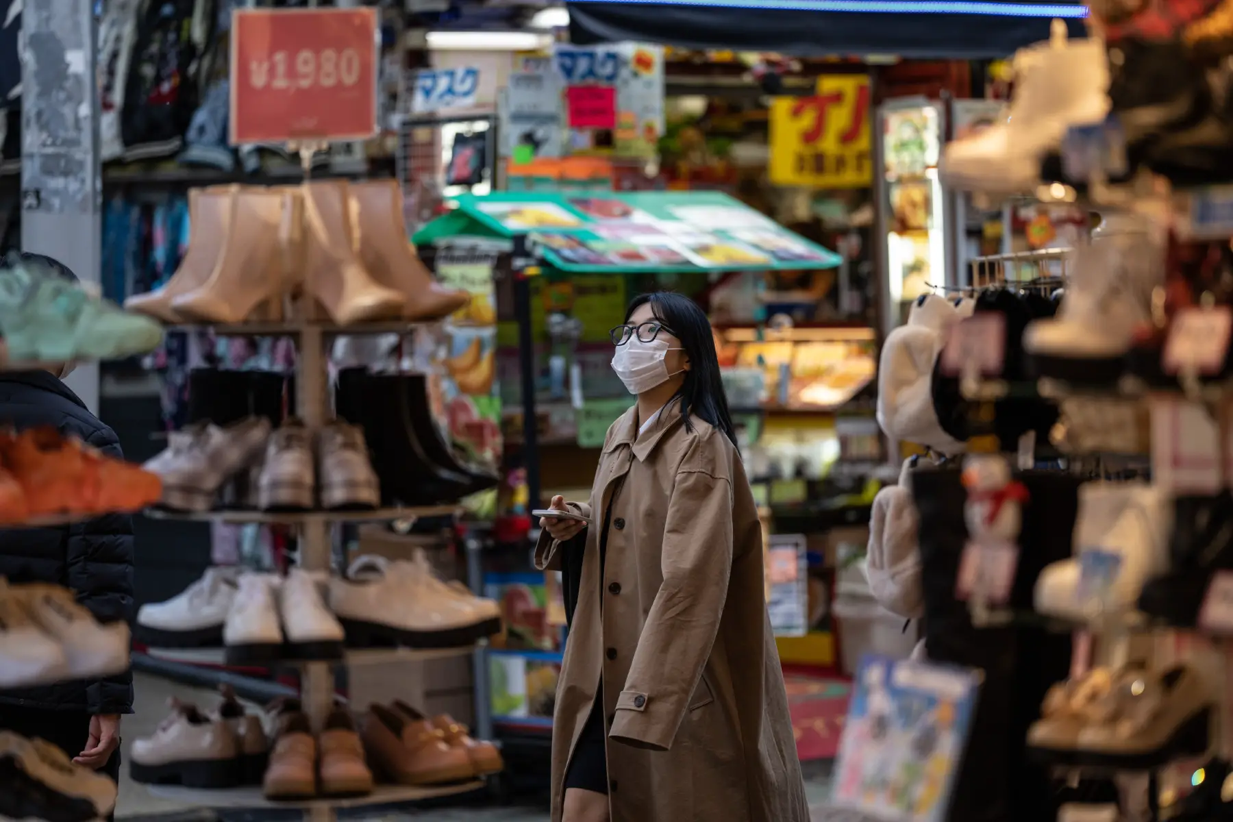 Woman wearing face mask and holding phone walks past shoe shop in Tokyo, Japan.