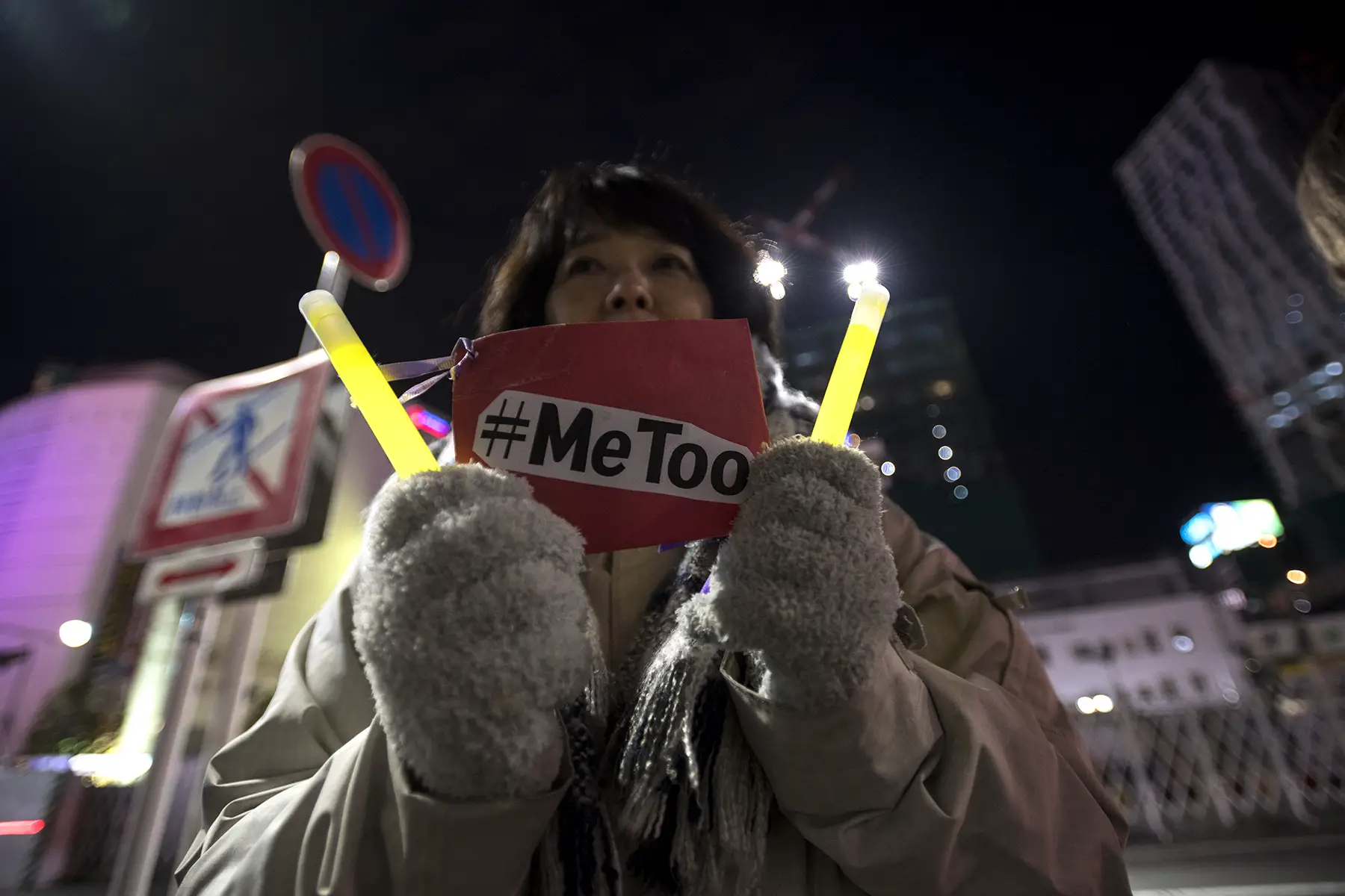 A woman holds up a #MeToo sign and two glowsticks at a women's rights protest