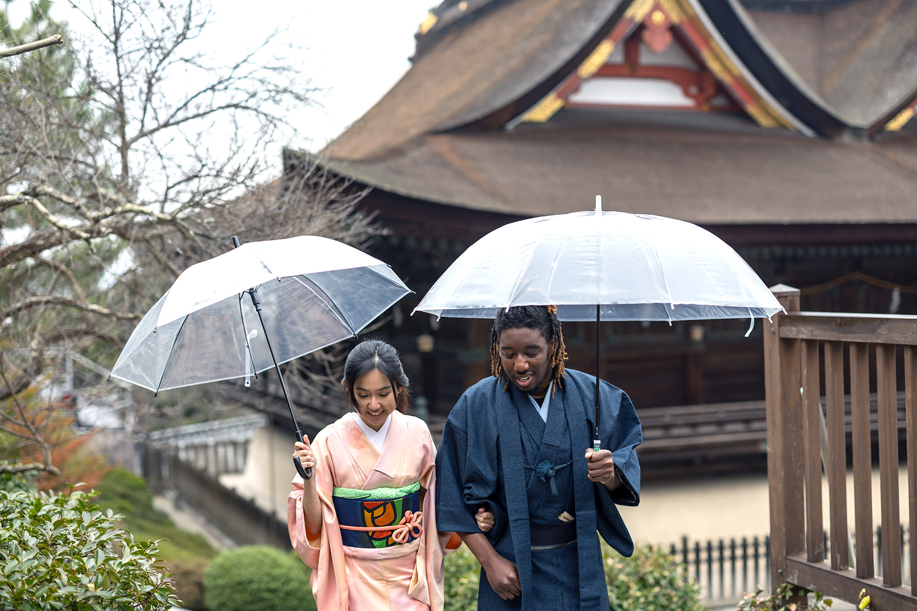 Cute couple wearing kimonos, walking arm in arm through the rain, holding umbrellas.