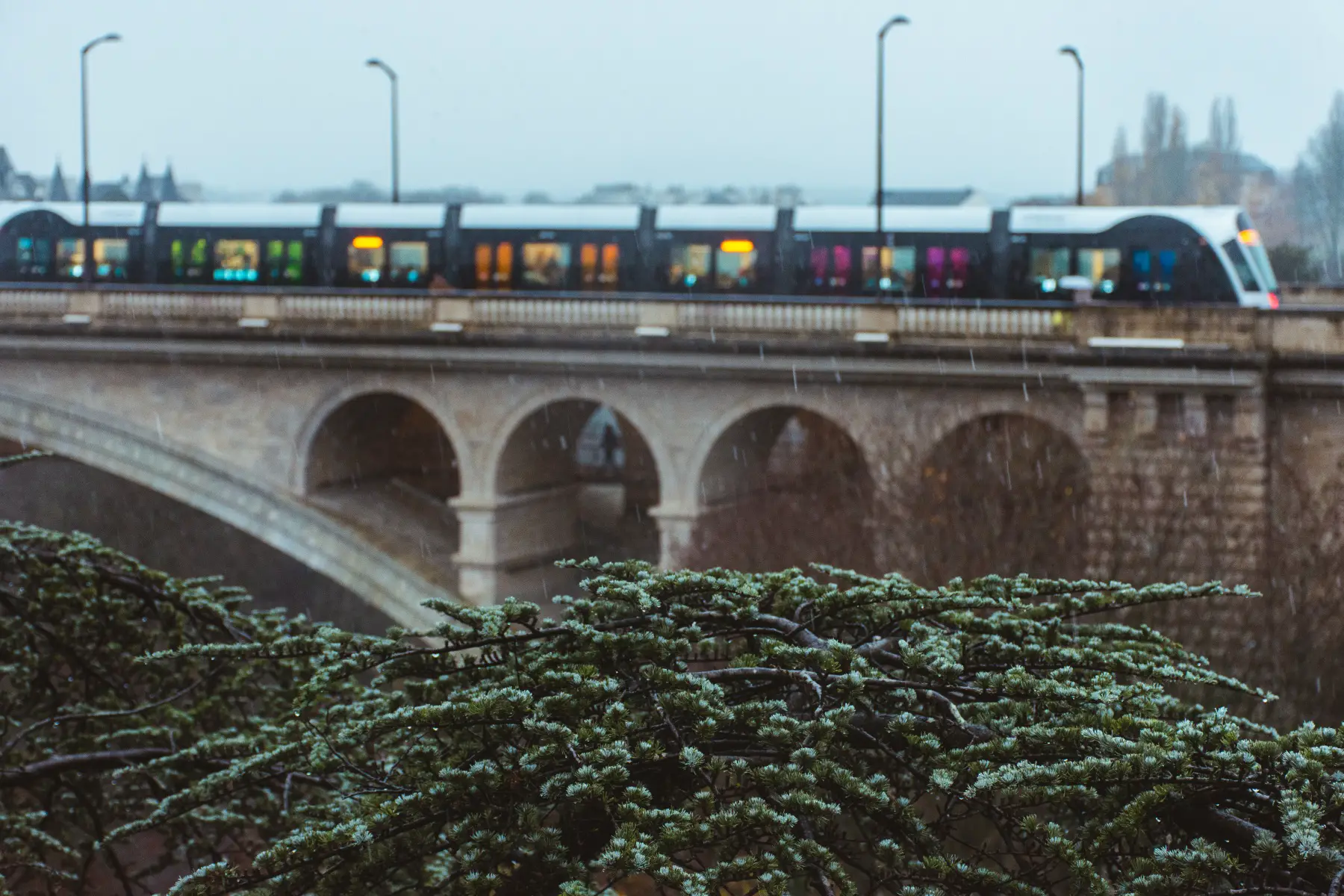 a train traveling over Adolphe Bridge on a snowy day in Luxembourg City