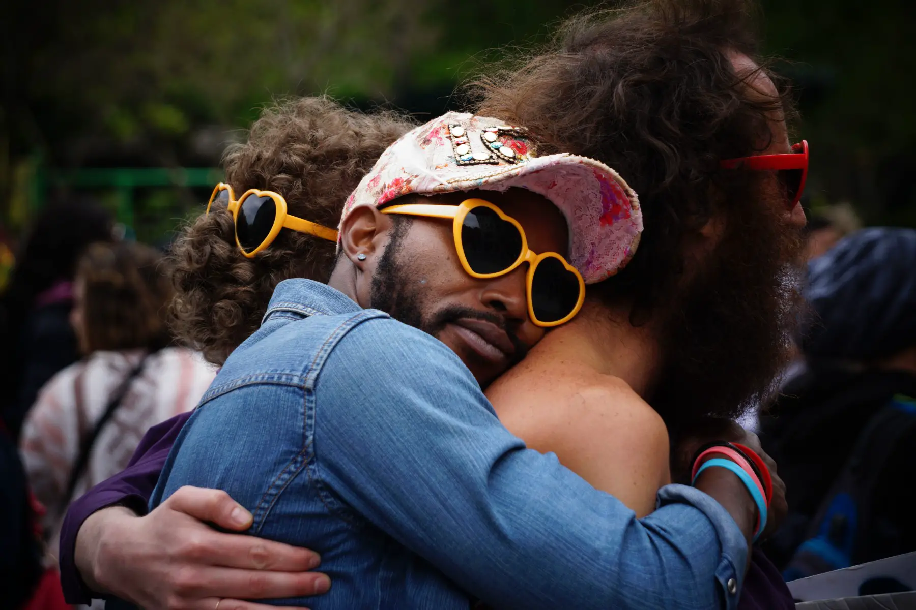 Friends or lovers embraced in a tight hug. They're all wearing heart-shaped sunglasses.